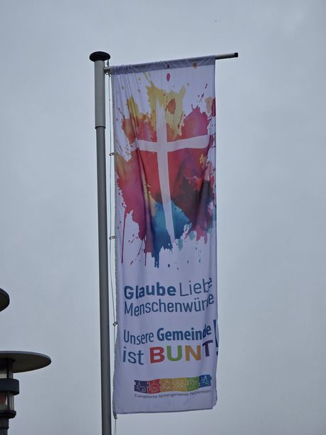 Colorful banner on a pole reading “Glaube liebt Menschenwürde… Unsere Gemeinde ist BUNT!”