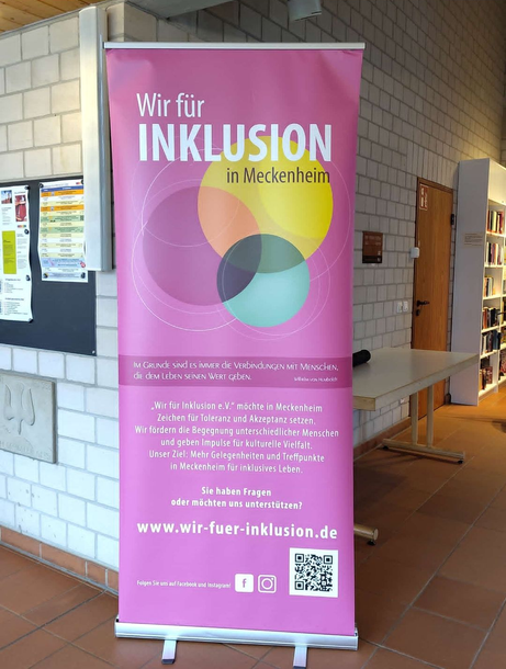 Pink “Wir für Inklusion in Mönchengladbach” banner with three overlapping circles, displayed indoors