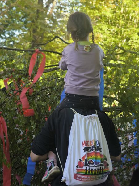 Ein Kind sitzt auf den Schultern eines Erwachsenen befestigt rote Bänder an Ästen vom Maibaum.