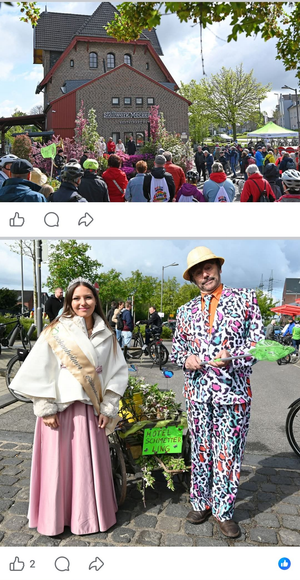 Zwei Personen in farbenfroher Tracht bei einem Freiluftfest, im Hintergrund eine Menschenmenge und eine Windmühle.