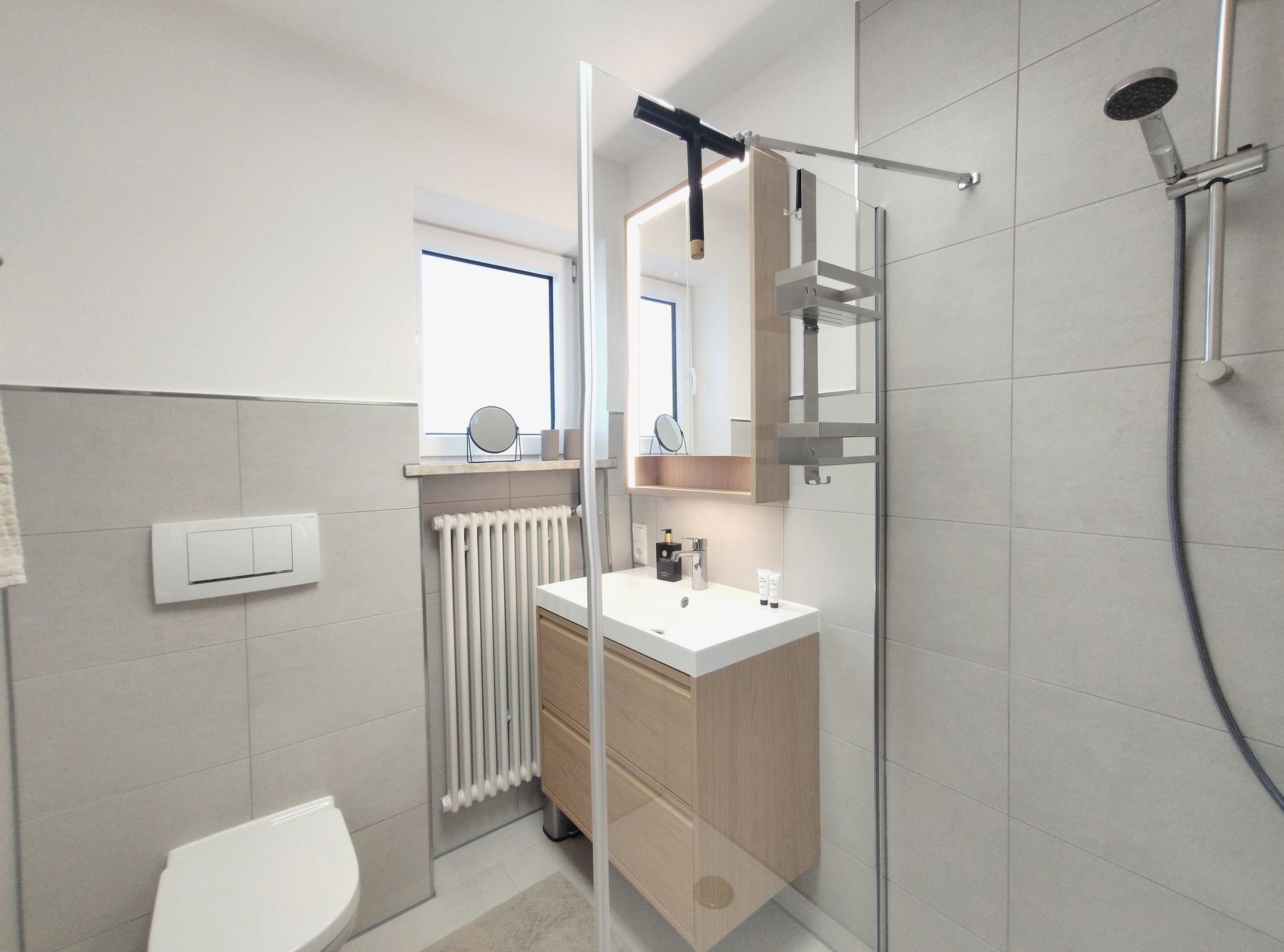 Modernes Badezimmer mit Dusche, Waschbecken, Toilette, Heizkörper und gefliesten Wänden