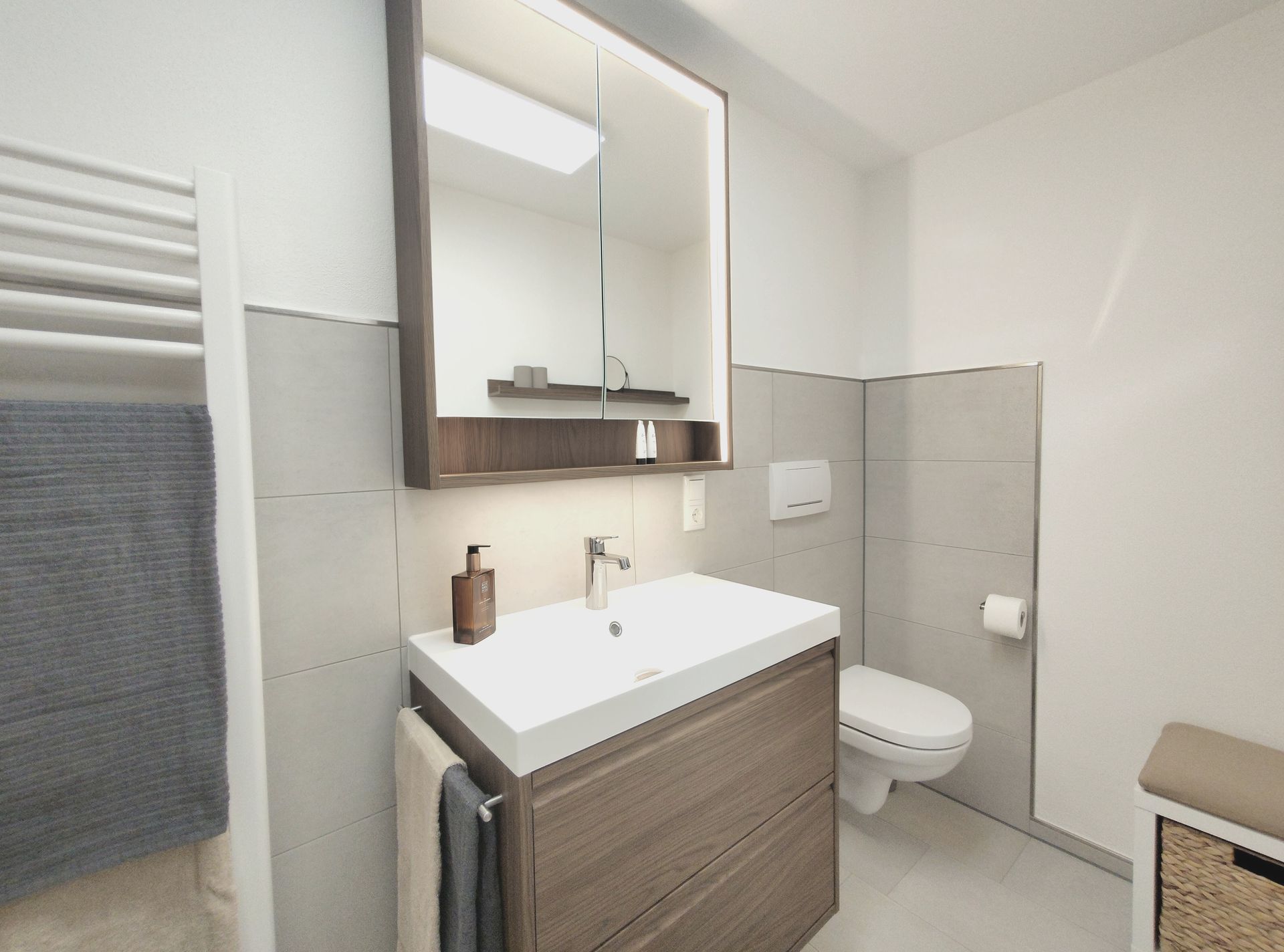 Modernes weißes Badezimmer mit Waschtisch, Spiegelschrank, Toilette und Handtuchheizkörper