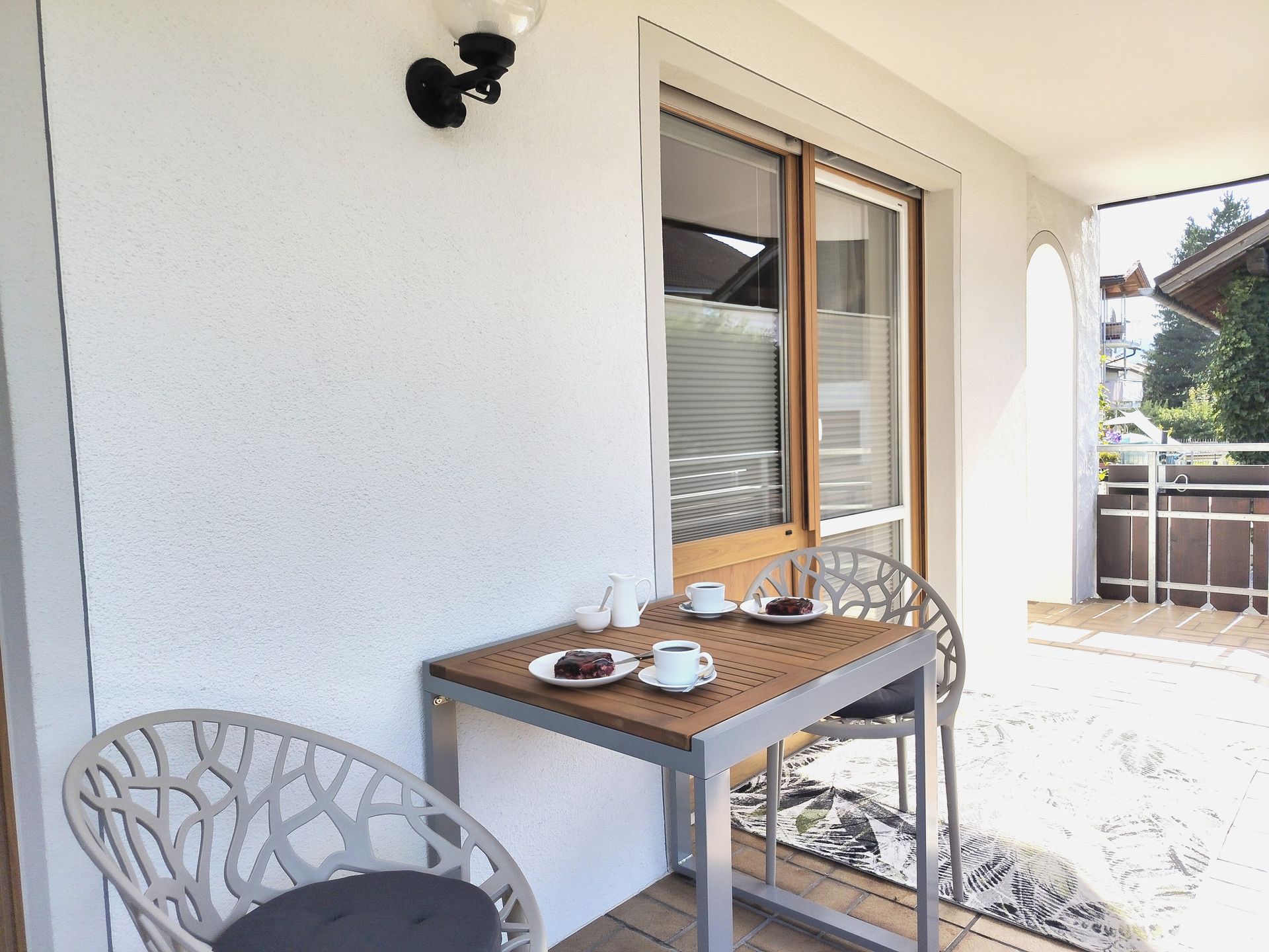 Eine Terrassentischgarnitur mit Teetassen und Stühlen steht neben einer Glastür auf einem überdachten Balkon.