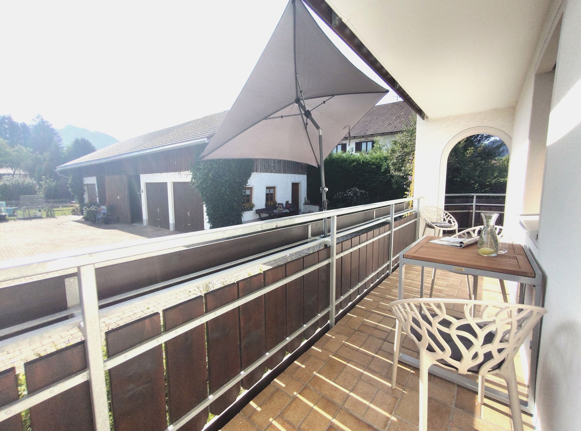 Balkongang mit weißen Stühlen, Holzterrasse und Bergblick neben modernen Gebäuden