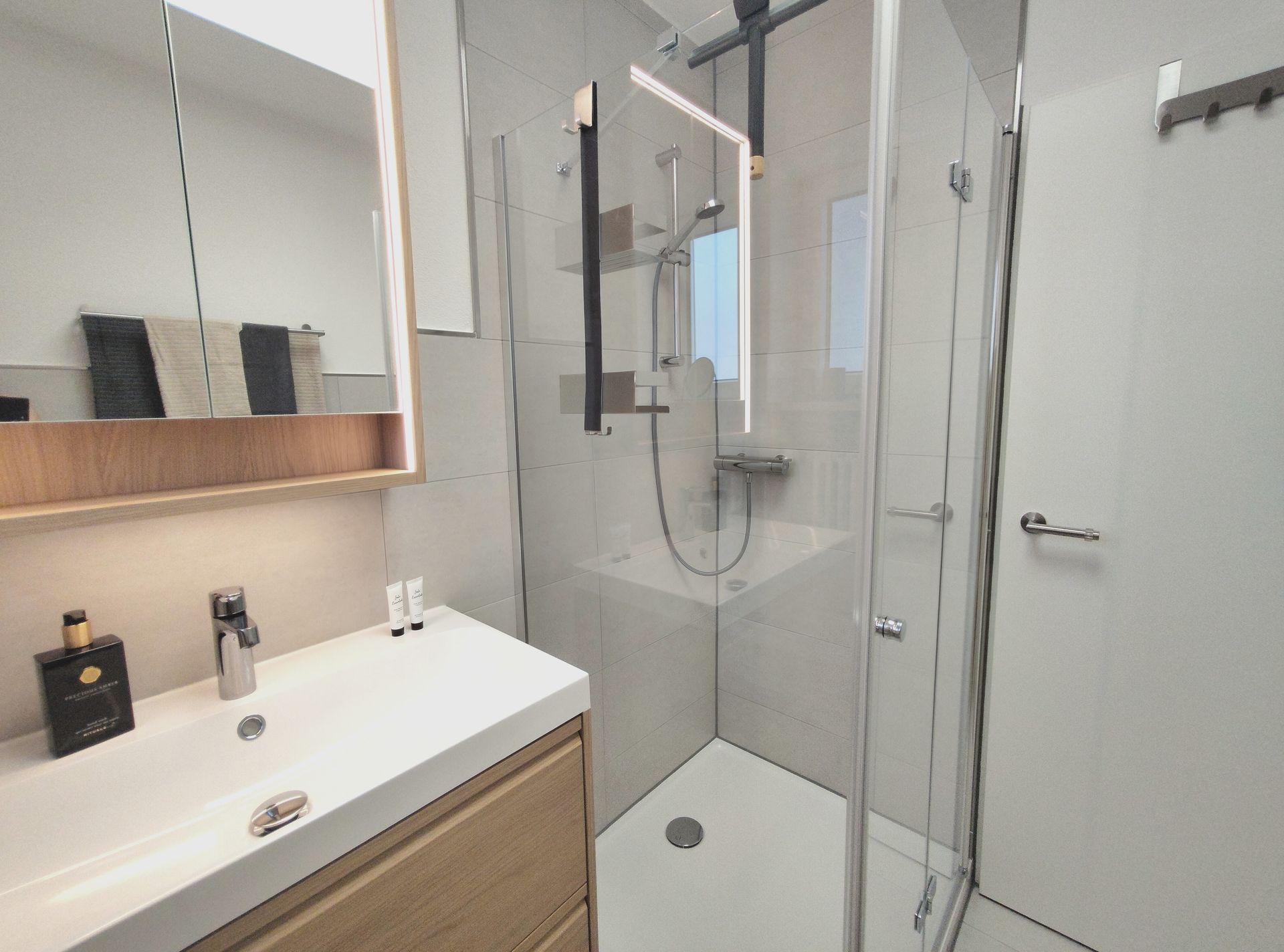 Modernes Badezimmer mit Waschtisch, großem Spiegel und Glasduschkabine in neutralen Farbtönen