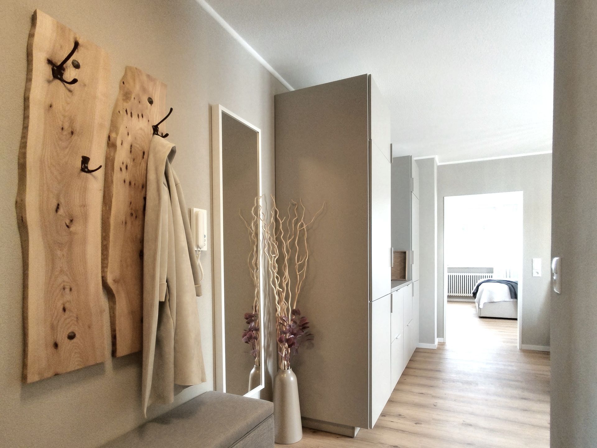 Moderner Flur mit Wandbildern, Garderobe, hoher Vase und einem hellen Schlafzimmer in der Ferne