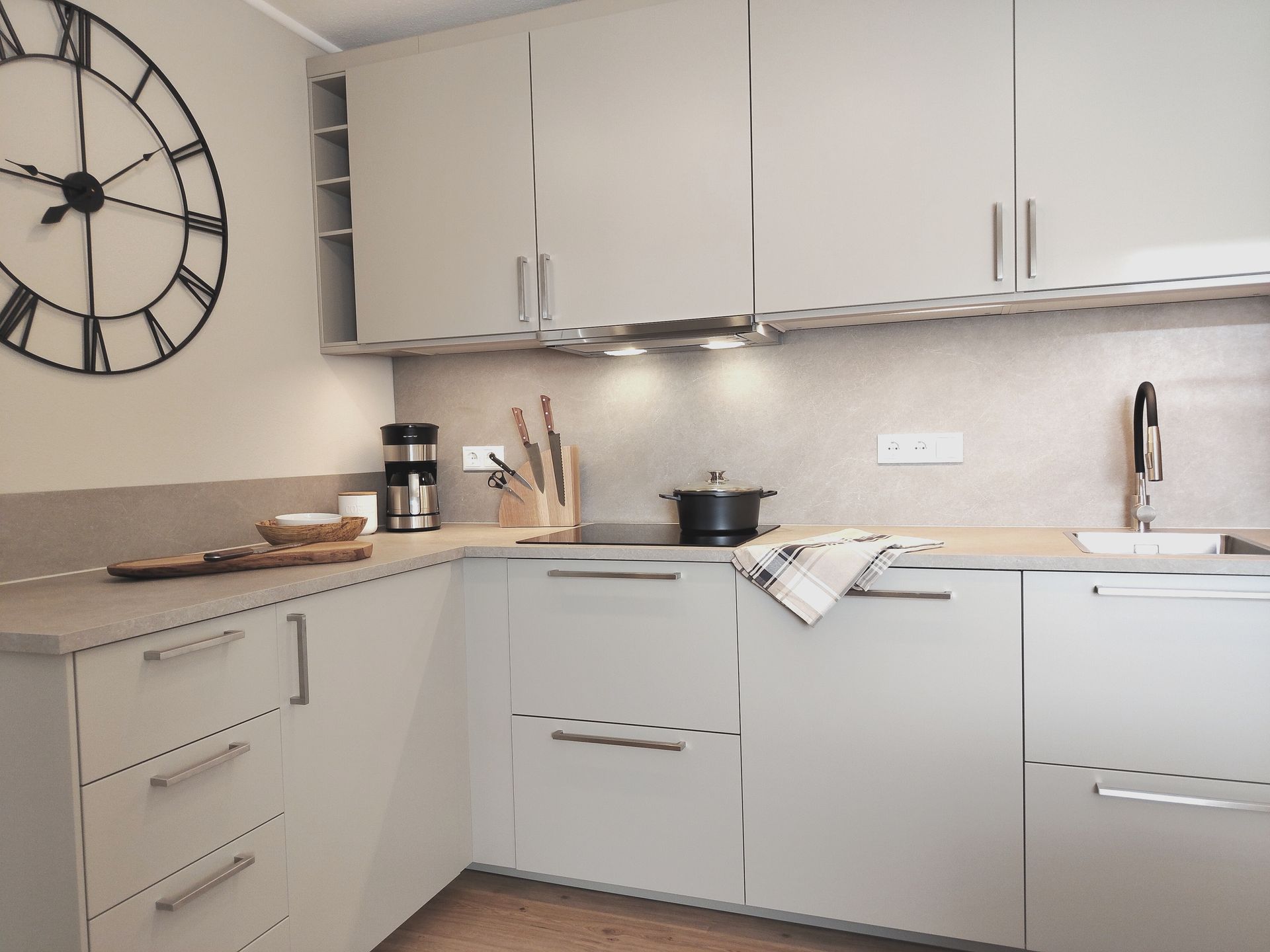Moderne Küche mit beigen Schränken, weißen Geräten, Arbeitsplatten und einer großen Wanduhr.