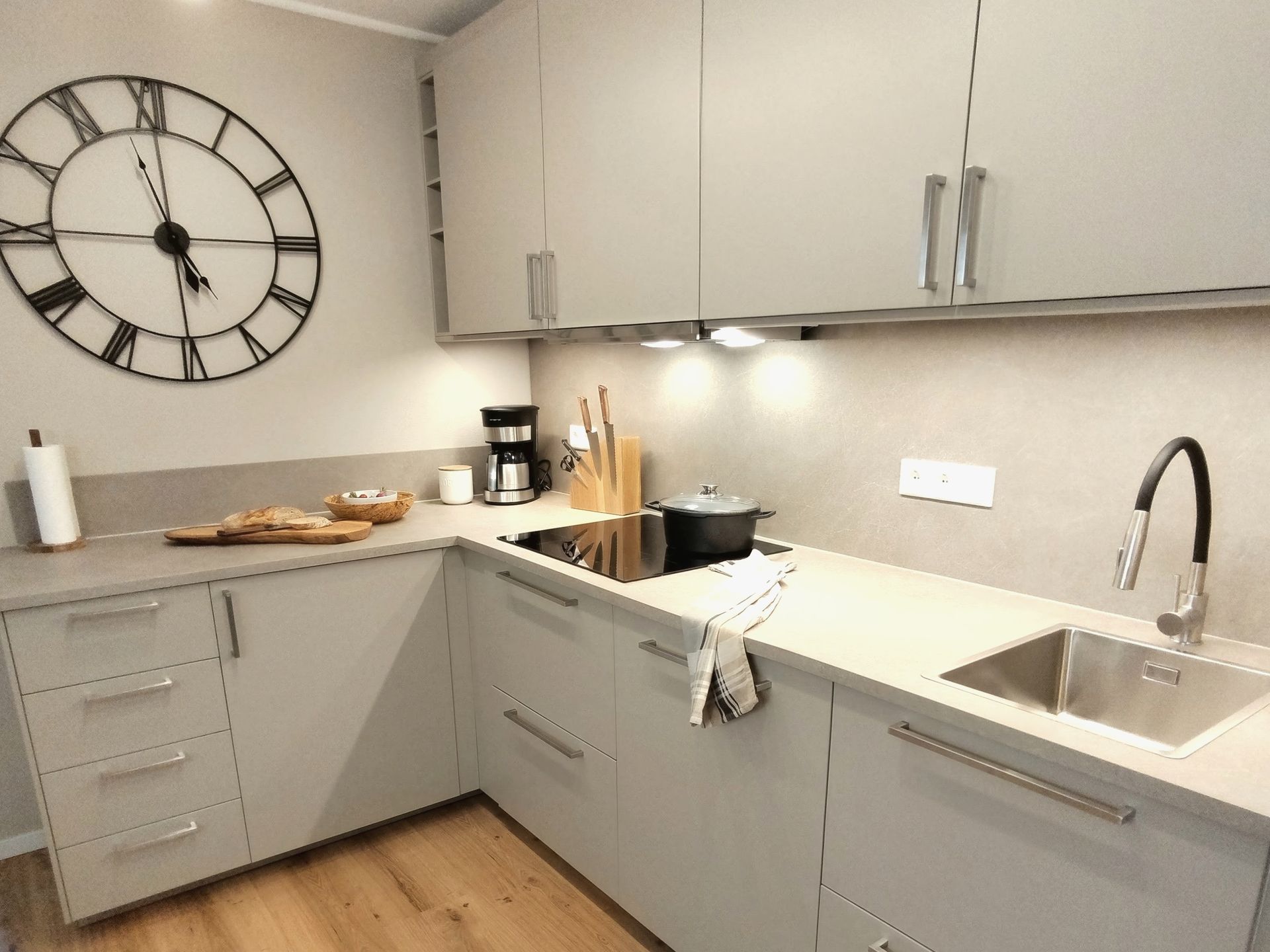 Moderne graue Küche mit L-förmiger Arbeitsplatte, Wanduhr, Spüle und kleinen Küchengeräten