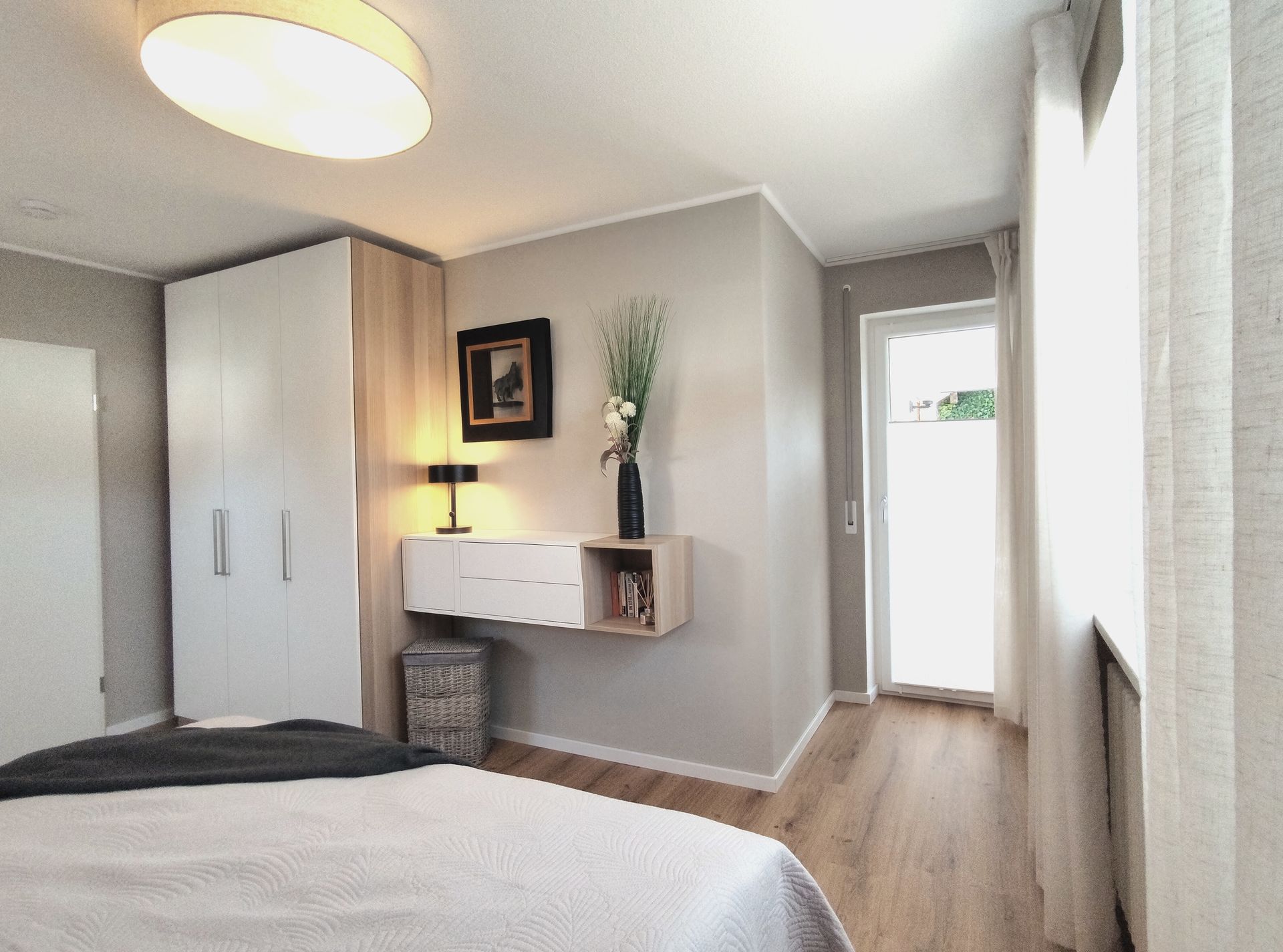 Helles, modernes Schlafzimmer mit Bett, Kleiderschrank, Schreibtischnische und Fensterlicht