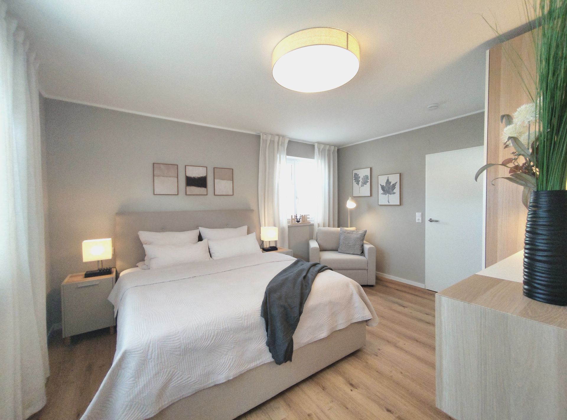 Helles Schlafzimmer mit großem Bett, grauer Sitzecke und Holzboden