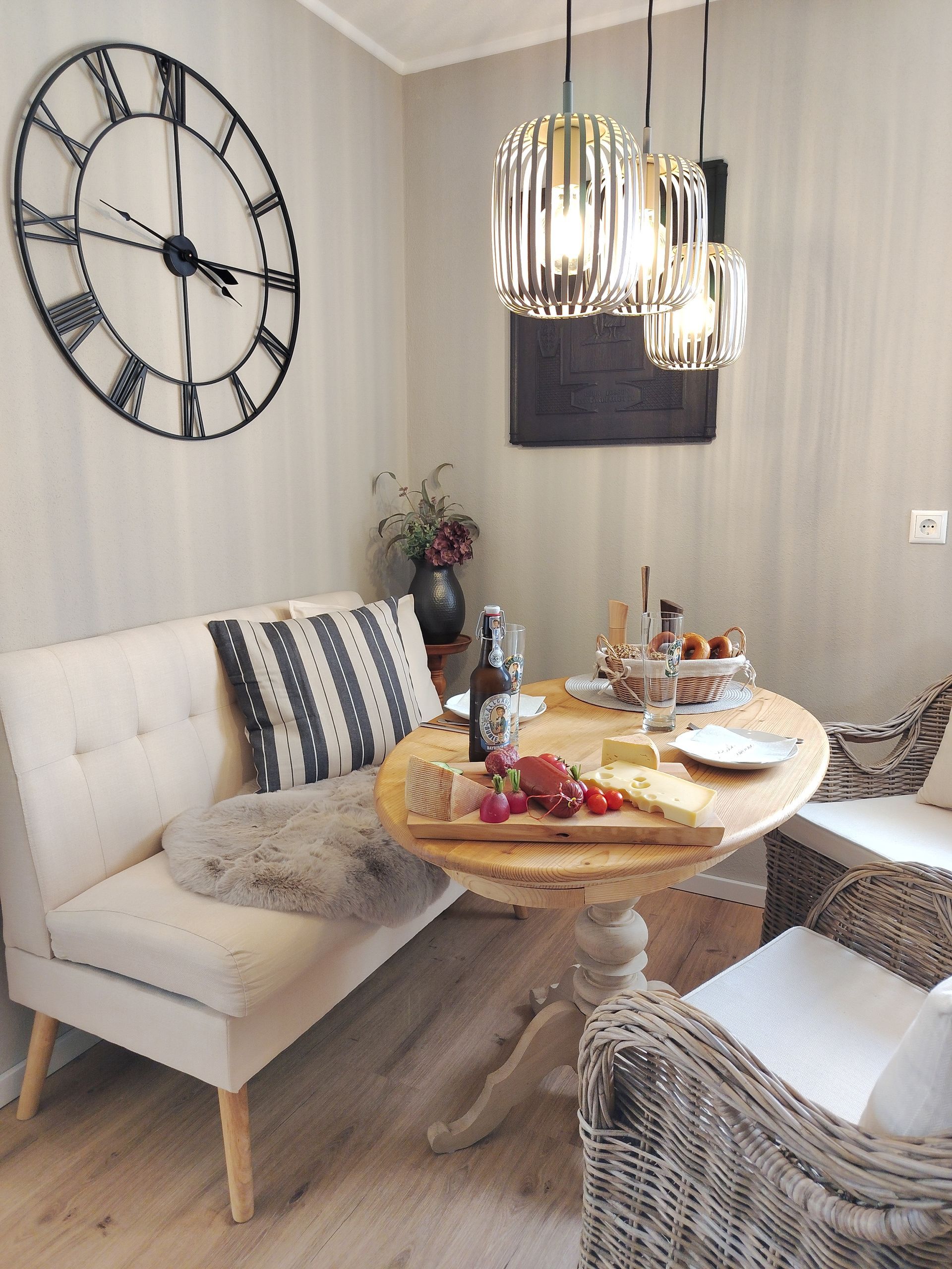 Gemütliche Essecke mit rundem Esstisch, weißem Sofa, Korbsessel und großer Wanduhr