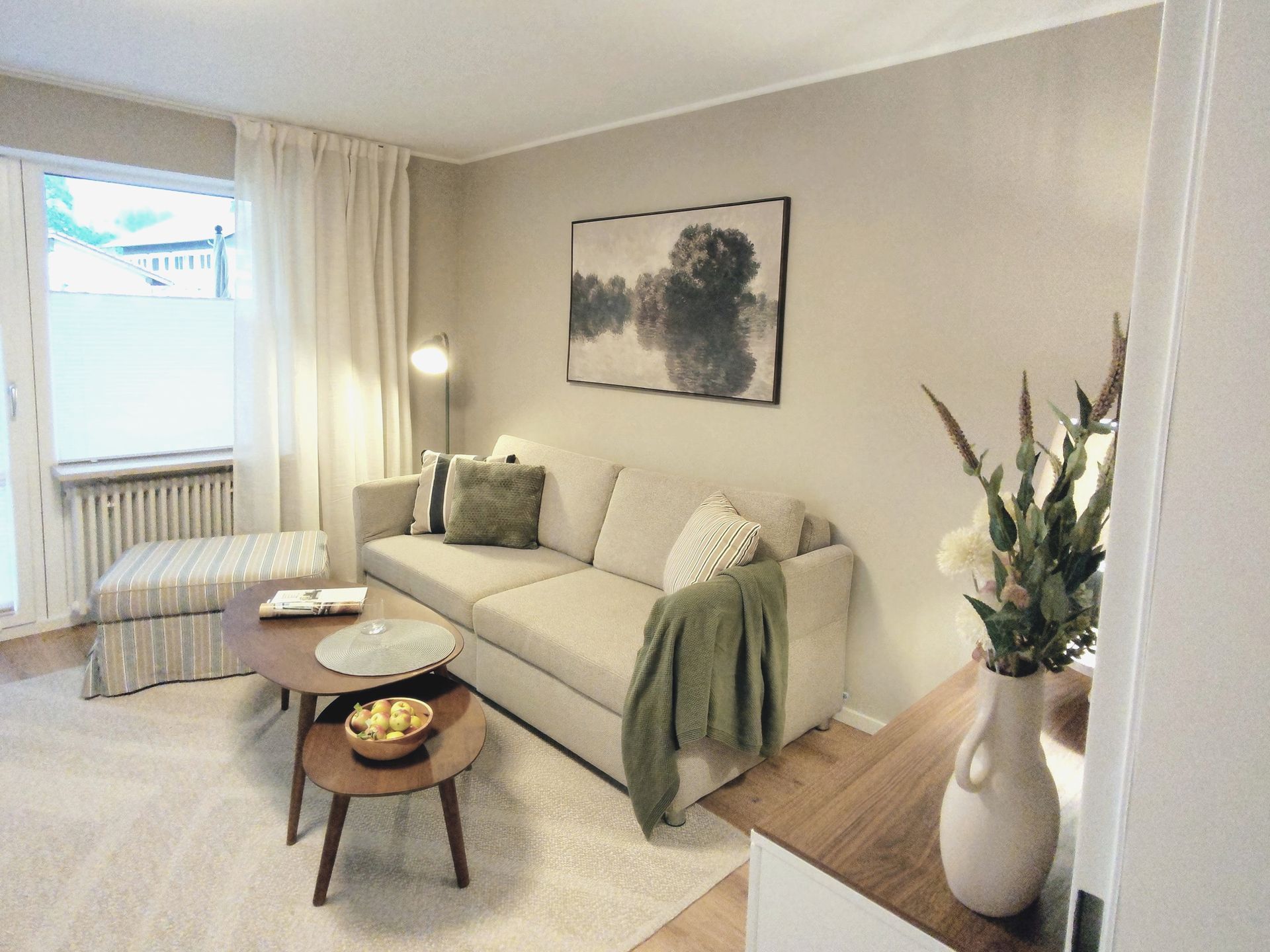 Helles, modernes Wohnzimmer mit beigefarbenem Sofa, Couchtisch, Stehlampe und Blumenvase am Fenster
