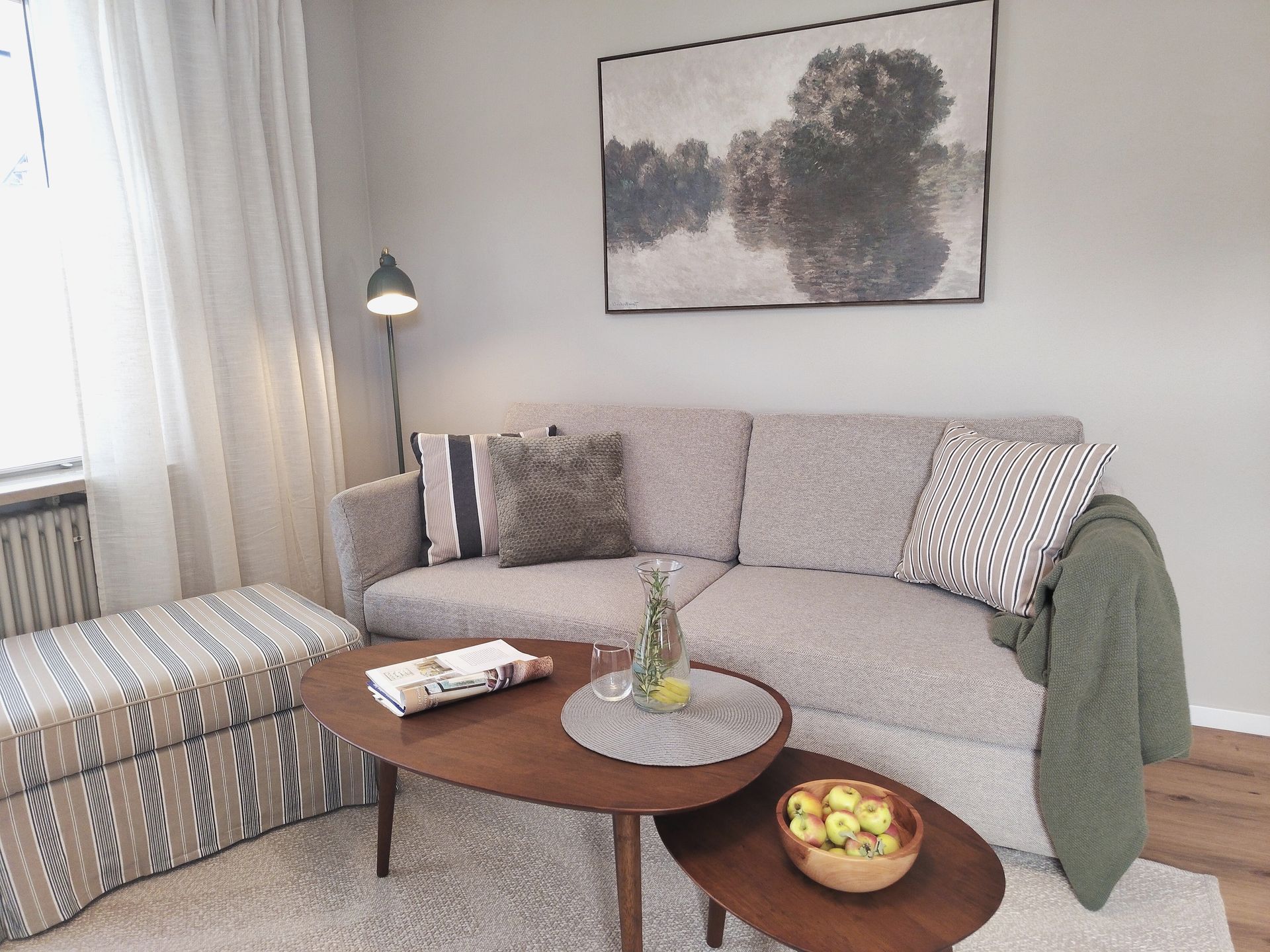 Gemütliches Wohnzimmer mit grauem Sofa, gemustertem Hocker, Couchtisch aus Holz und abstrakter Wandkunst.