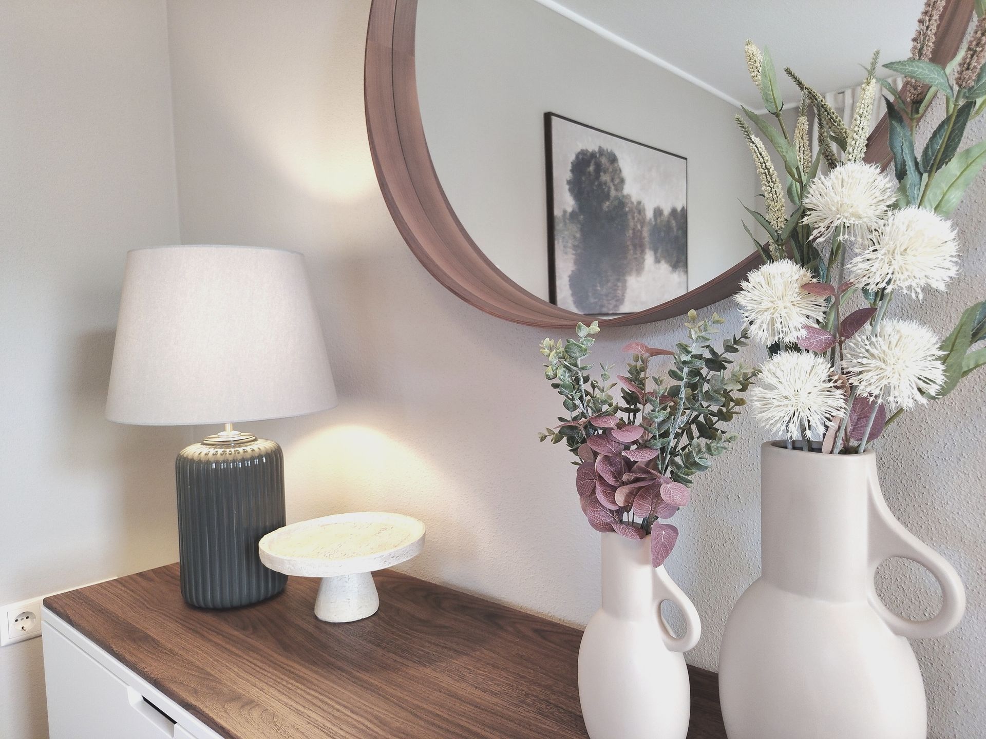 Stilvoller Konsolentisch mit Lampe, Spiegel und weißen Blumenvasen in einem hellen Raum