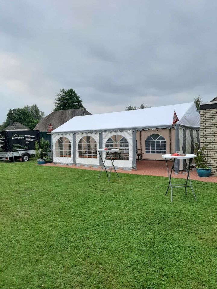 Auf einer Rasenfläche neben einem Gebäude und einem Catering-Anhänger steht ein großes weißes Festzelt mit Bogenfenstern.