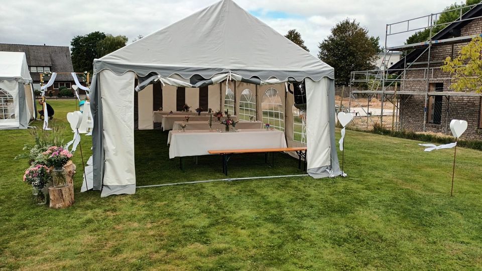 Ein weißes Festzelt, aufgestellt auf einer Rasenfläche, mit Tischen und Bänken im Inneren, dekoriert für eine Feier im Freien.