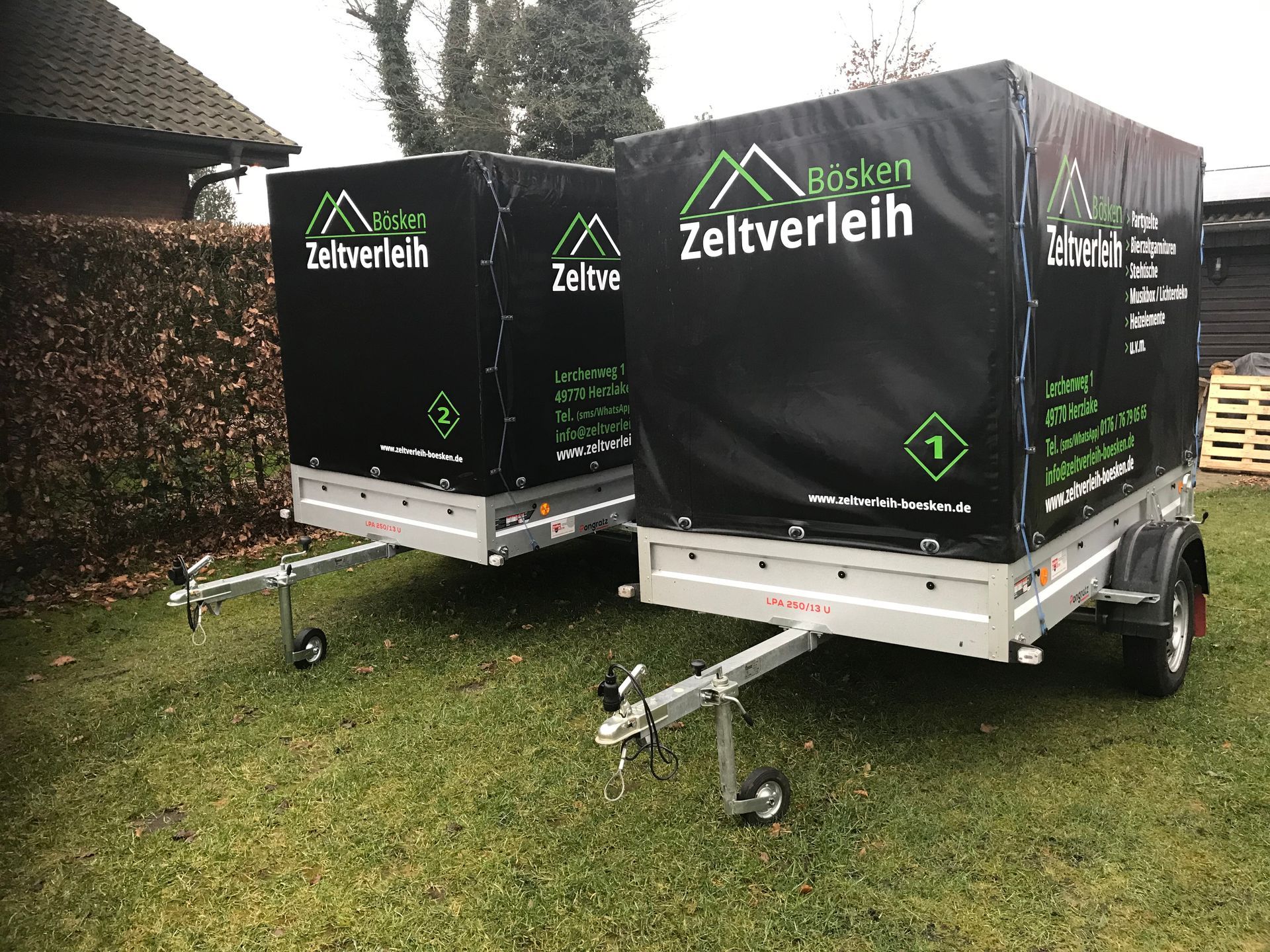 Zwei schwarze Anhänger mit grüner Aufschrift parkten nebeneinander auf einer Rasenfläche.