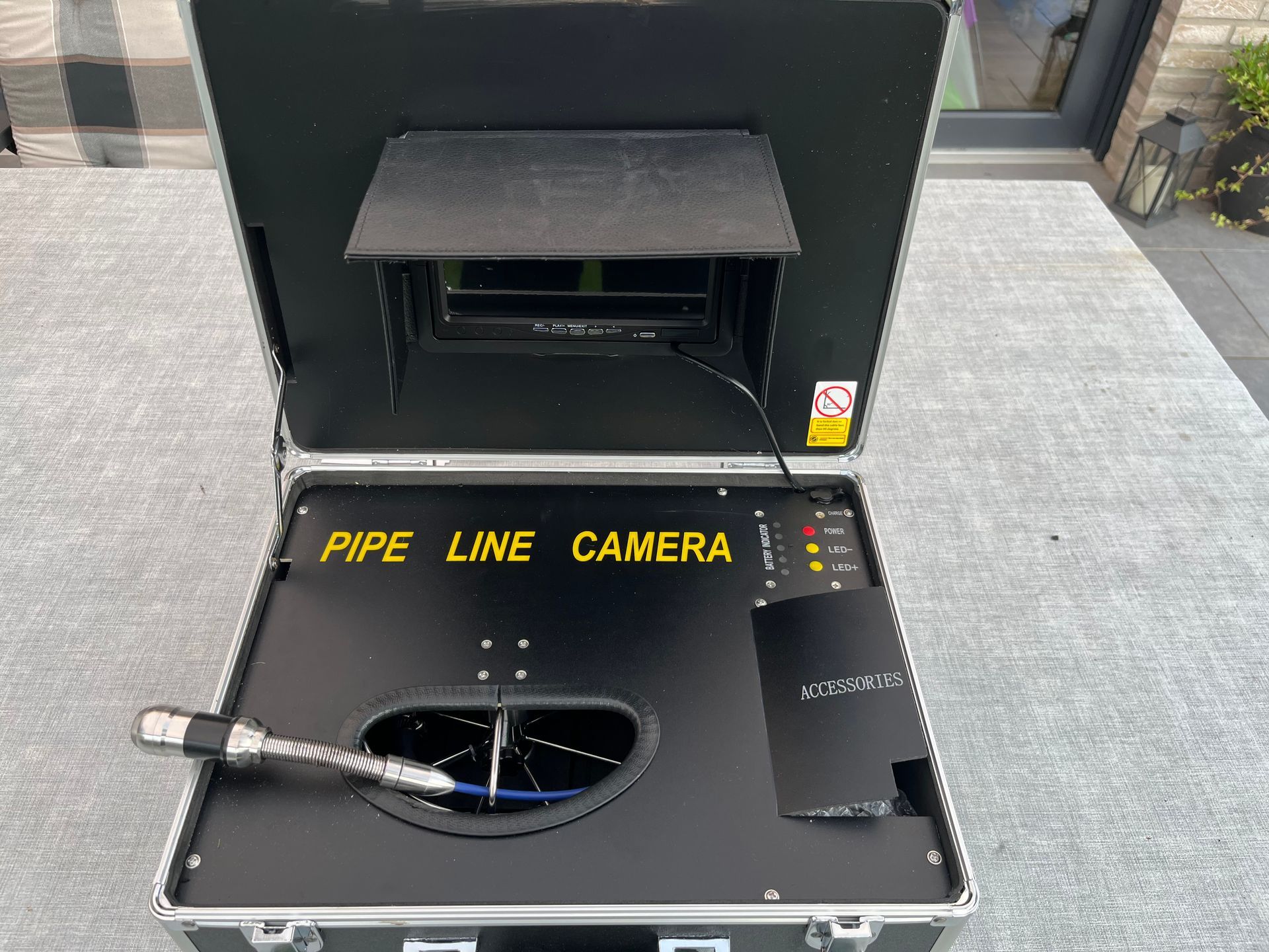 Ein tragbares Rohrinspektionskamera-Set in einem offenen silbernen Koffer, bestehend aus Monitor, Bedienfeld und Kamerakopf.