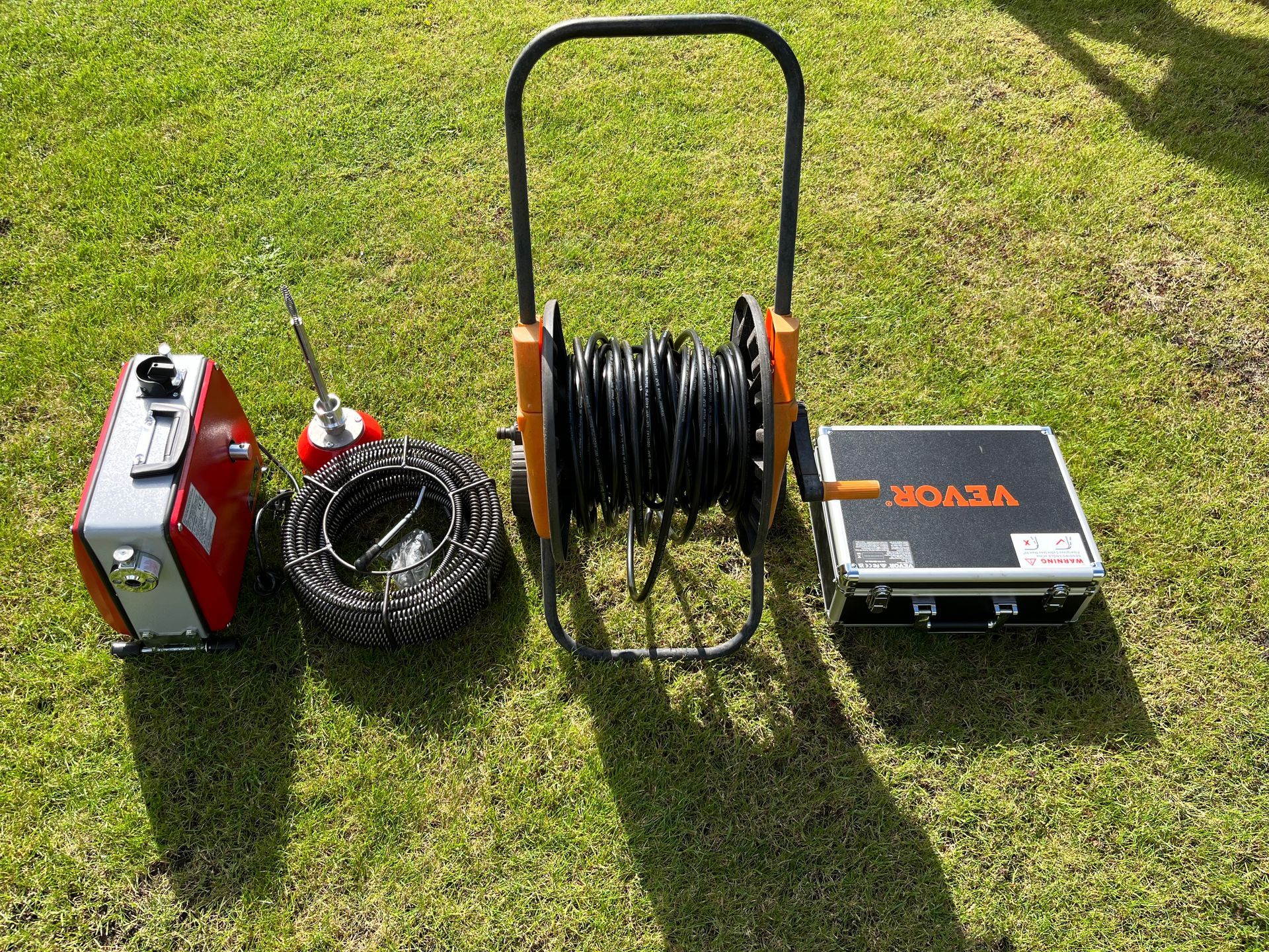 Ein Rohrinspektionskamerasystem mit Monitor, Kabeltrommel, Kabel und Steuereinheit auf grünem Rasen.