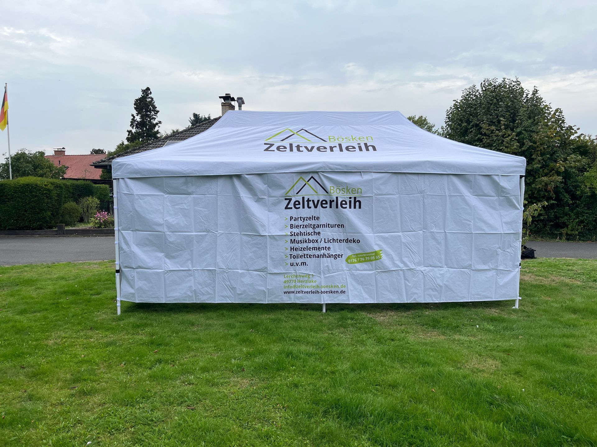 Ein großes, weißes Festzelt mit Giebeldach und bogenförmigen, gitterförmigen Fenstern, das auf einer Rasenfläche aufgebaut ist.