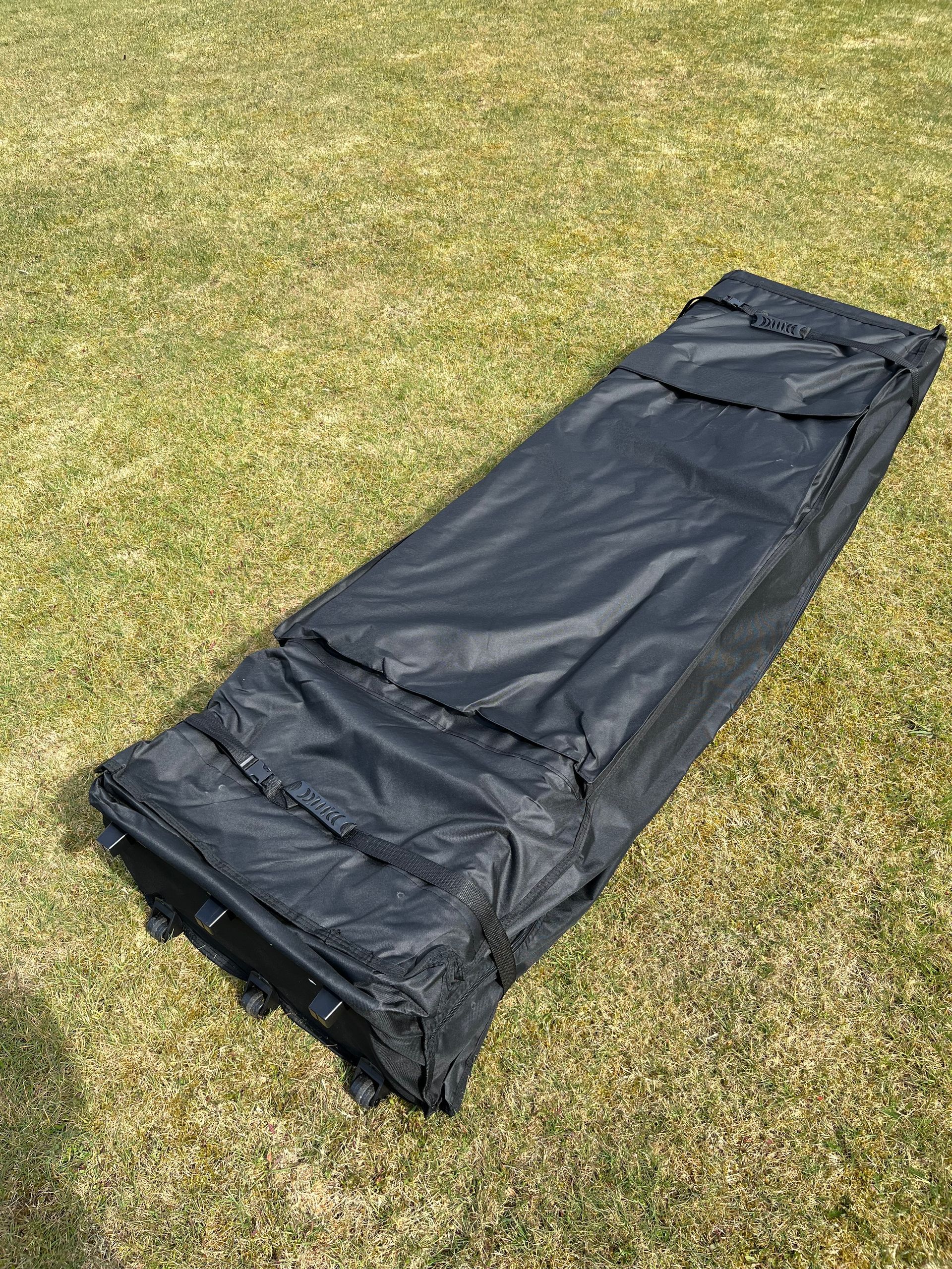 Eine schwarze, rechteckige, rollbare Ausrüstungstasche liegt auf einer Wiese.