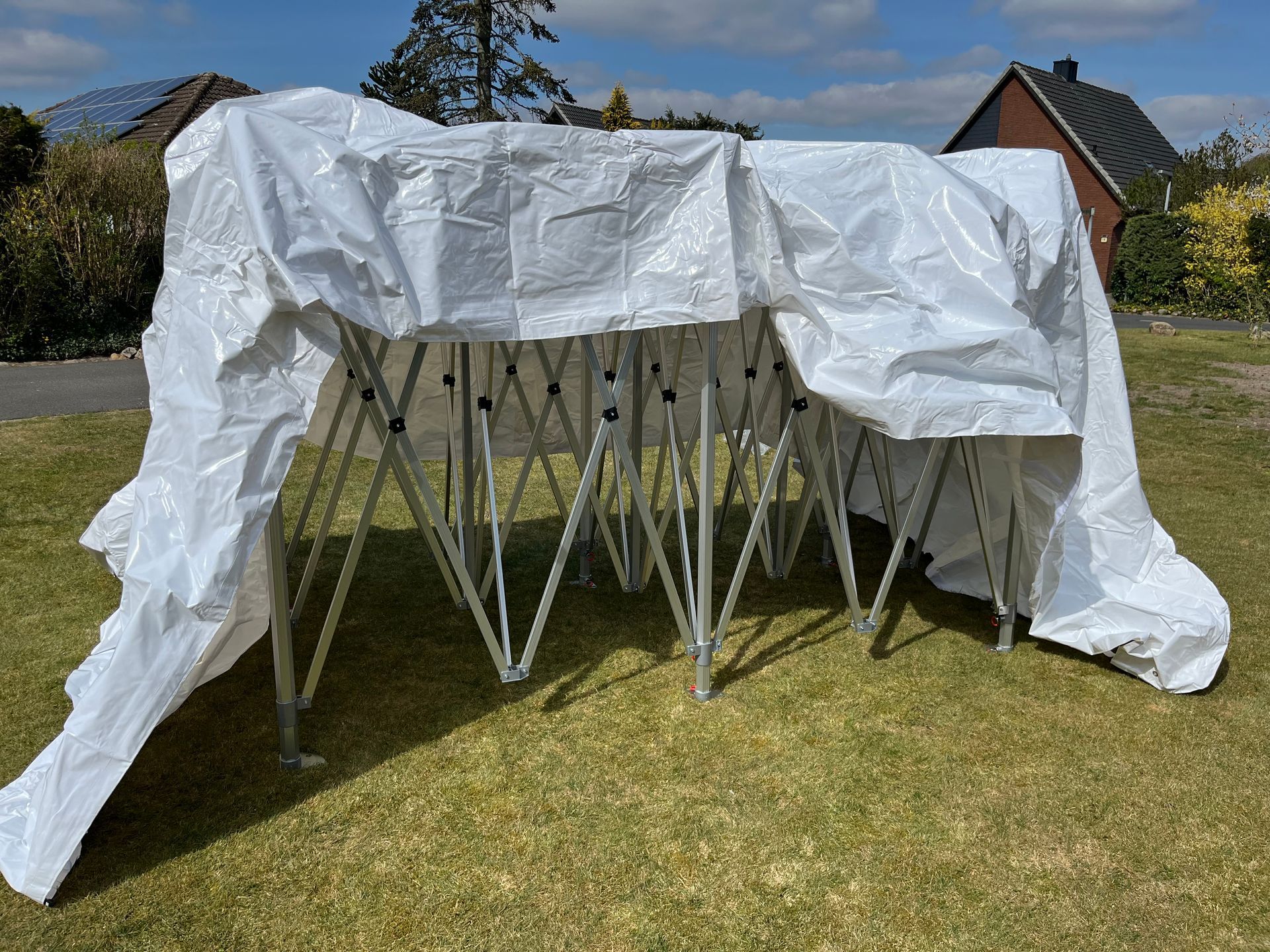 Eine weiße Plane war über ein teilweise aufgebautes, ausziehbares Metallrahmen-Pavillon drapiert, das auf einer Rasenfläche aufgestellt war.