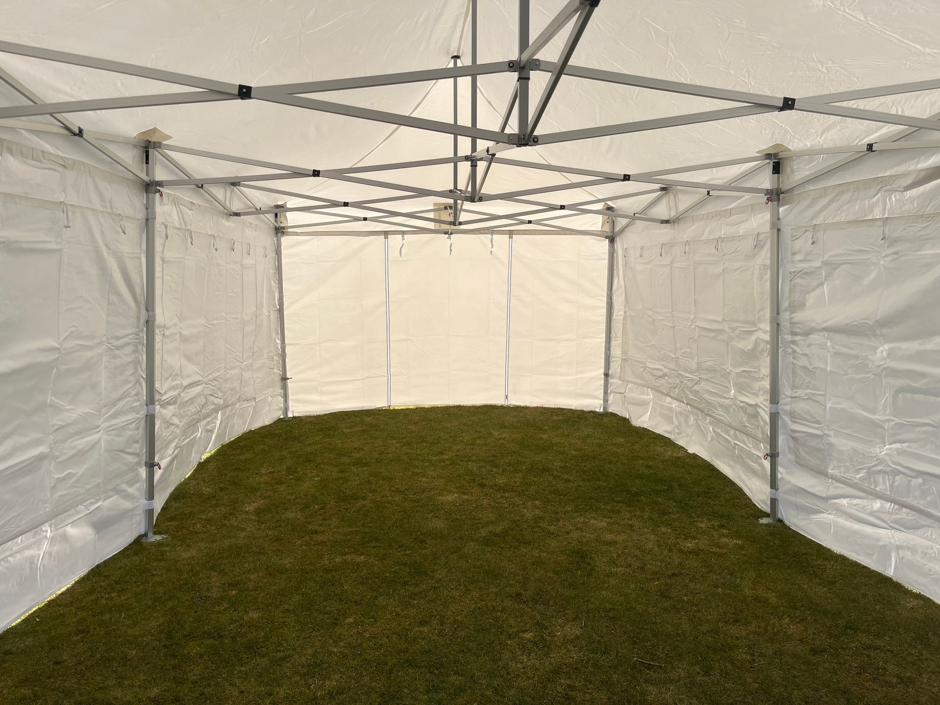 Ein leeres, weißes Pop-up-Veranstaltungszelt, das auf einer Rasenfläche aufgebaut ist; Blick von innen auf die Rückwand.