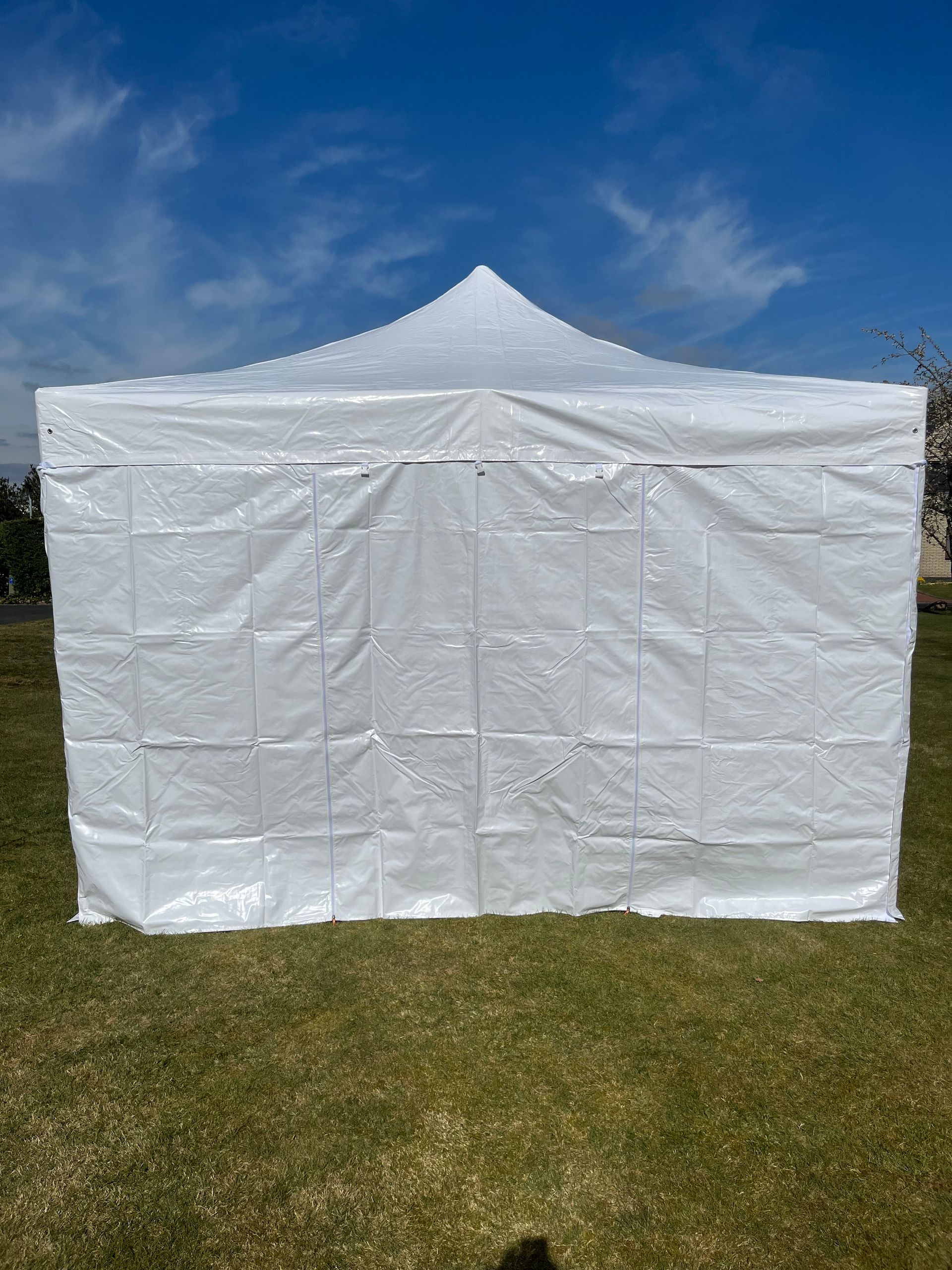 Ein weißes, quadratisches Faltpavillonzelt steht auf einem Stück grünem Rasen vor einem klaren blauen Himmel.