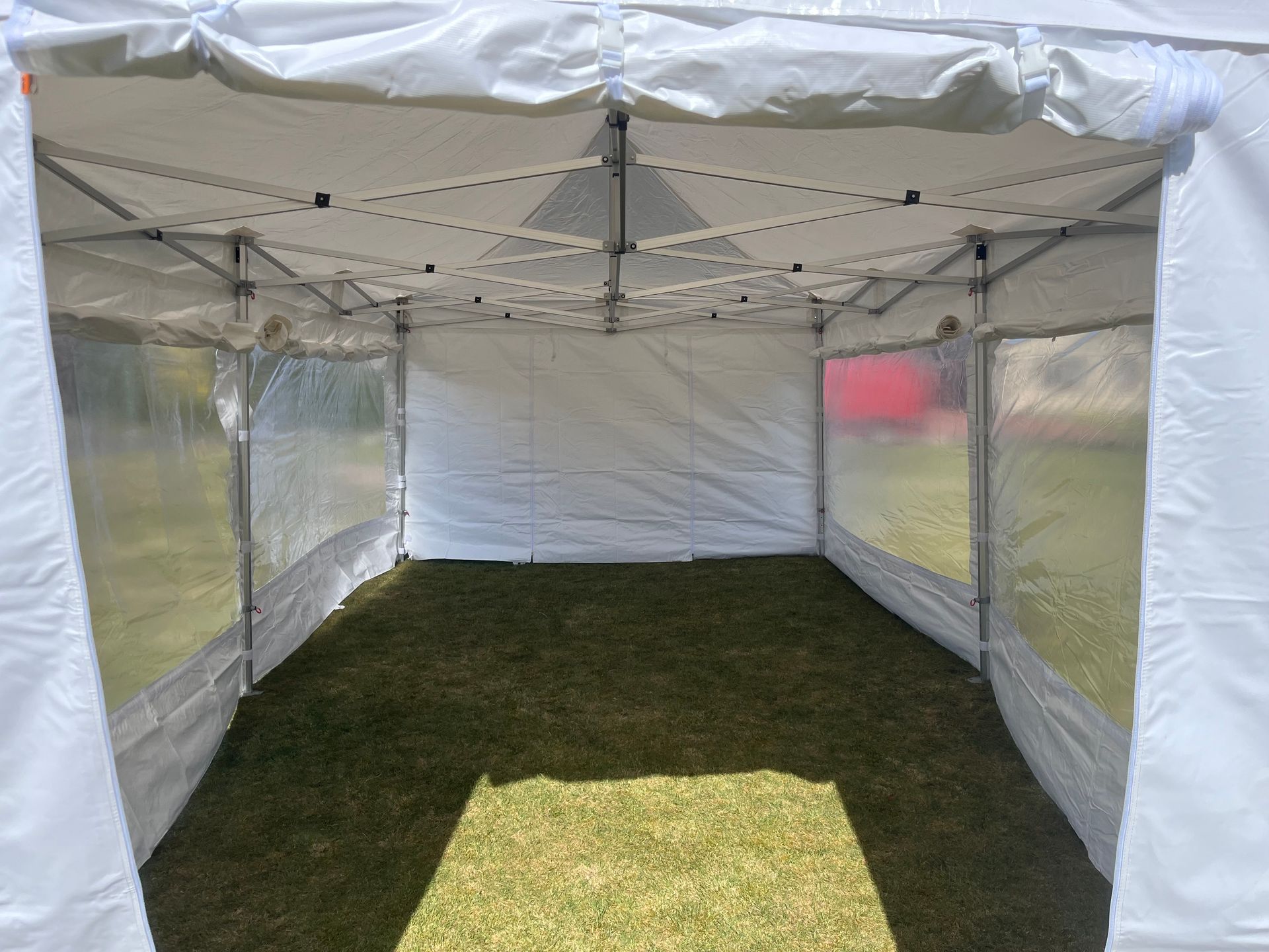 Im Inneren eines weißen, zusammenklappbaren Pop-up-Zeltes auf einer Rasenfläche, mit transparenten Seitenwänden und einer massiven weißen Rückwand.