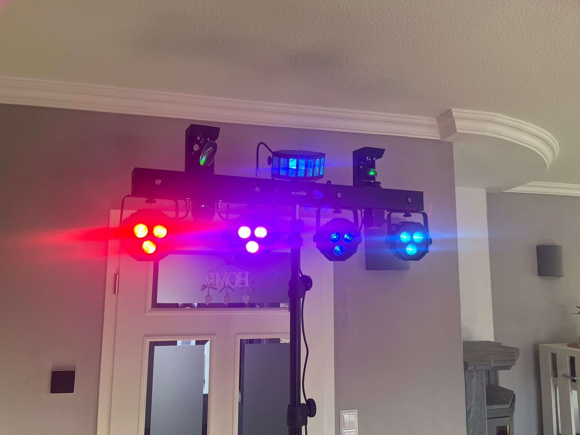 Ein Schwarzlichtständer mit vier Scheinwerfern und einer zentralen Kugel, der in Innenräumen in leuchtendem Rot, Lila und Blau erstrahlt.