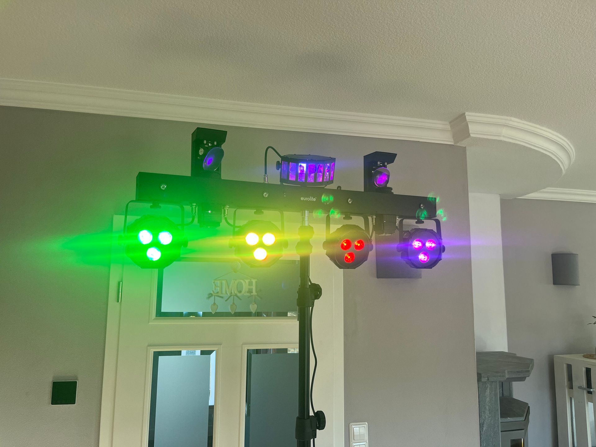 Eine auf einem Stativ montierte Bühnenbeleuchtungsleiste projiziert helle grüne, gelbe, rote und violette Lichtstrahlen in einen Raum.
