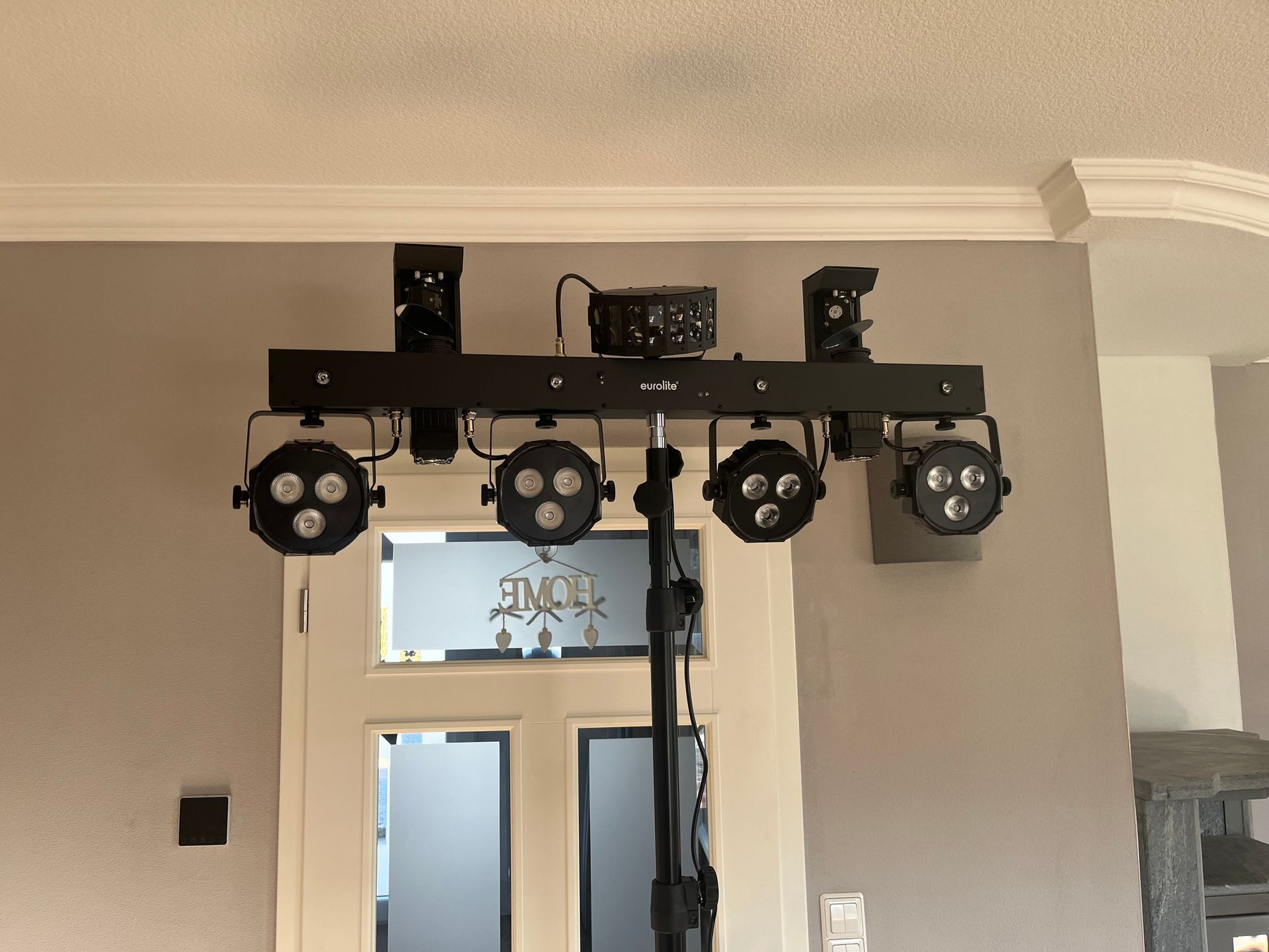 Ein schwarzes Lichtstativ mit vier runden LED-Bühnenscheinwerfern, die an einer horizontalen Stange vor einem weißen Türrahmen montiert sind.