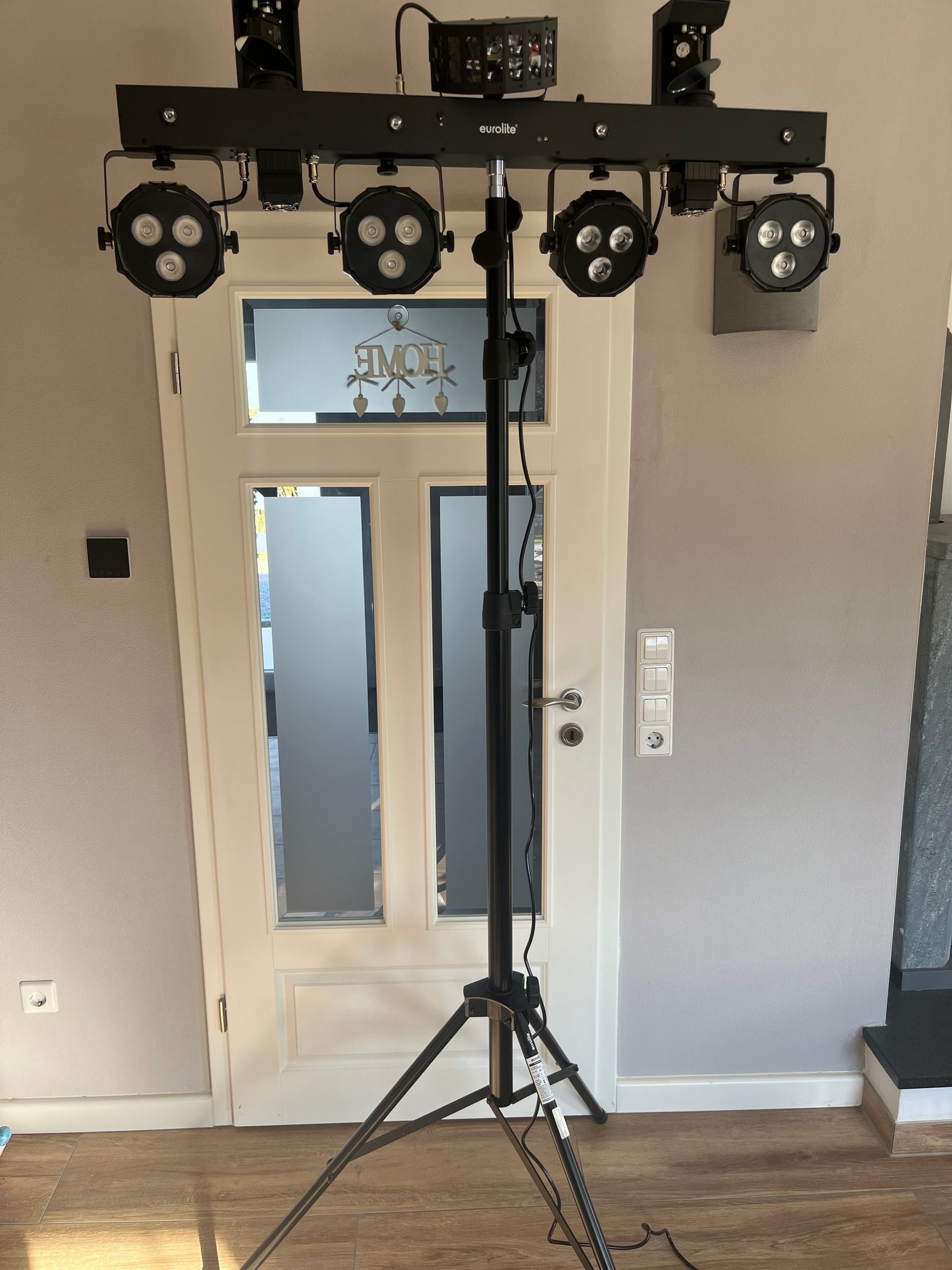Eine Bühnenbeleuchtungsanlage mit vier runden LED-Leuchten, die auf einem schwarzen Stativ vor einer weißen Innentür montiert sind.