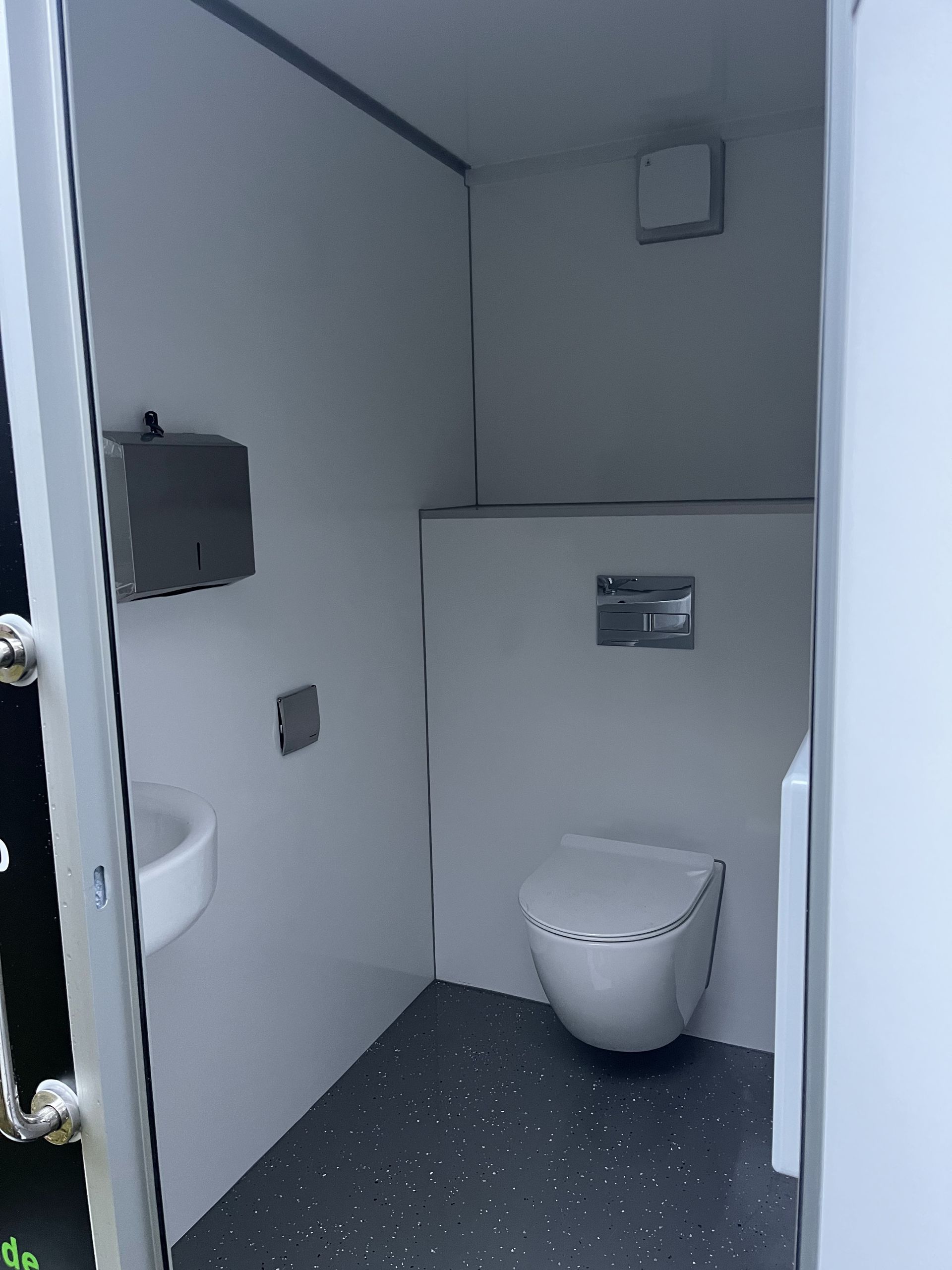 Eine kleine, moderne, weiße Einzeltoilette mit wandmontiertem WC, Waschbecken und Papierhandtuchspender.