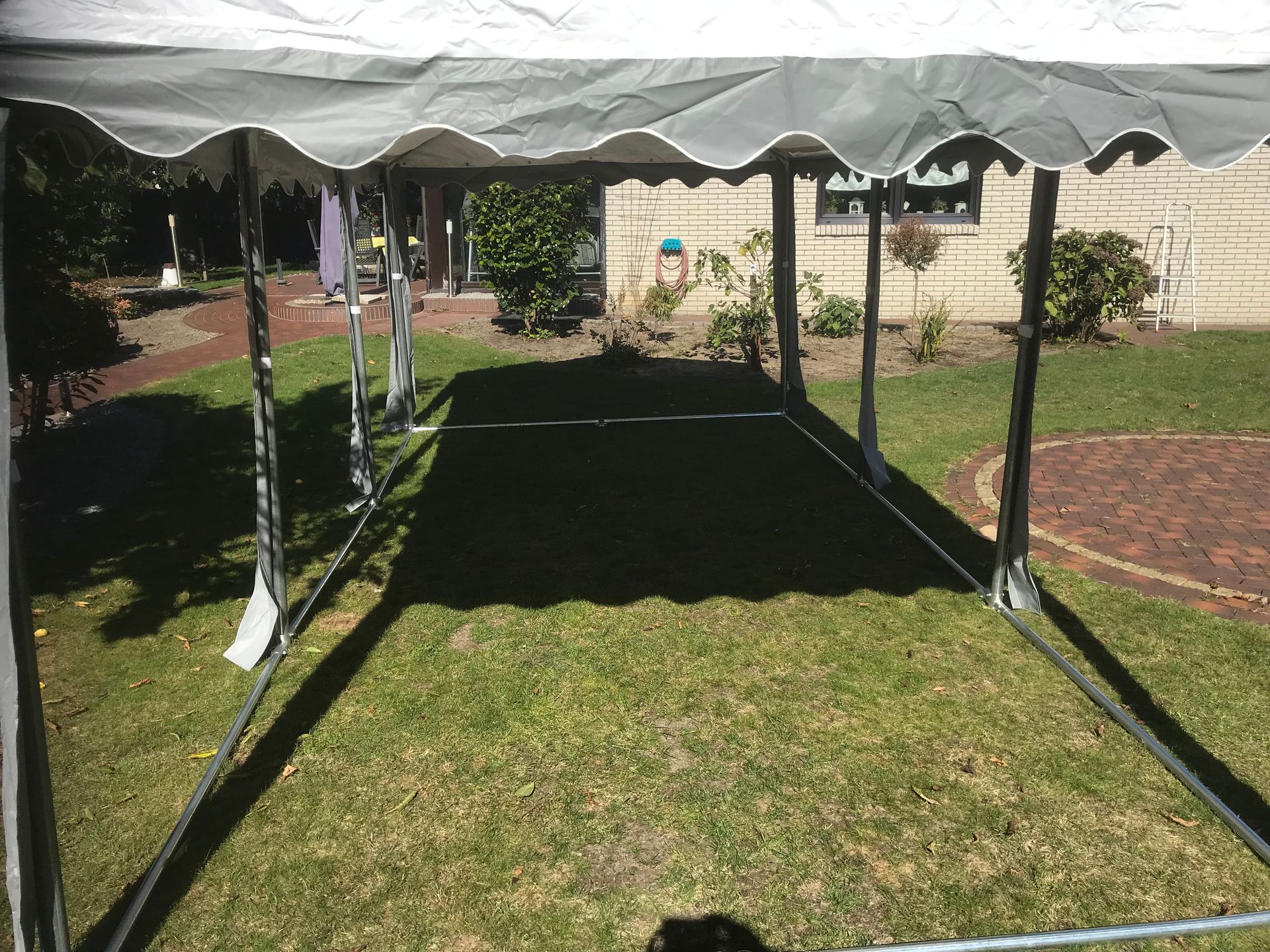 Ein weiß-graues Freiluftzelt steht auf einer grünen Rasenfläche, Blick von innen nach draußen.