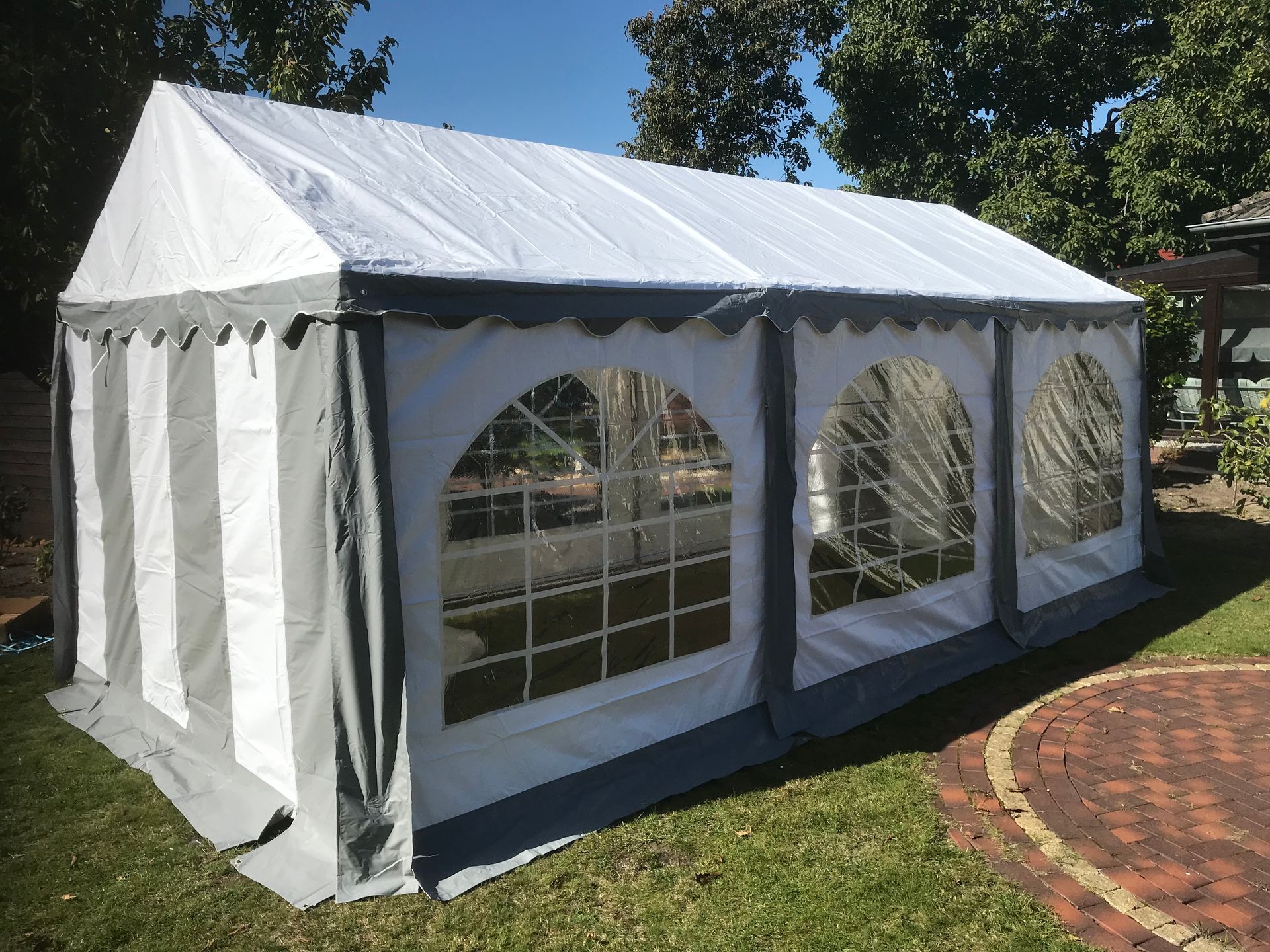 Ein großes, weißes Festzelt mit Giebeldach und bogenförmigen, gitterförmigen Fenstern, das auf einer Rasenfläche aufgebaut ist.