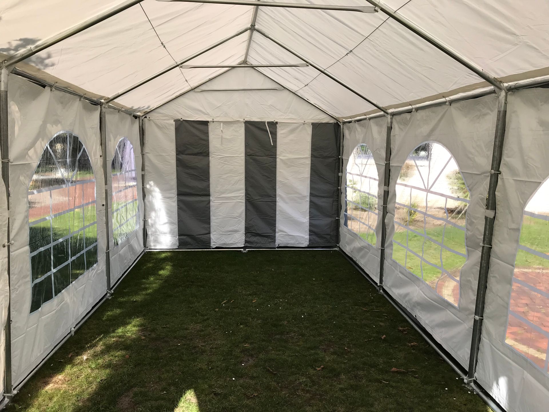 Ein leeres Partyzelt mit weißen und grauen Wänden und bogenförmigen, durchsichtigen Kunststofffenstern, das auf einer Rasenfläche aufgebaut ist.