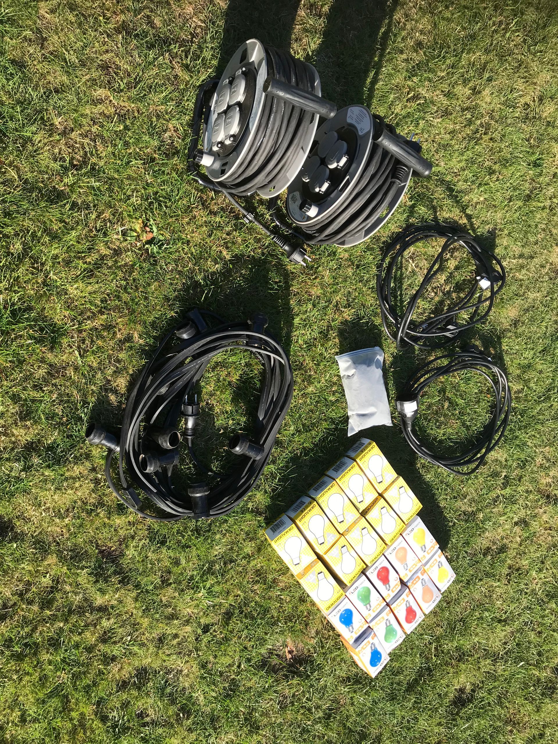 Eine Ansammlung von Lichterketten, Kabeln und mehreren Schachteln mit farbigen Ersatzglühbirnen, die auf dem Rasen arrangiert sind.