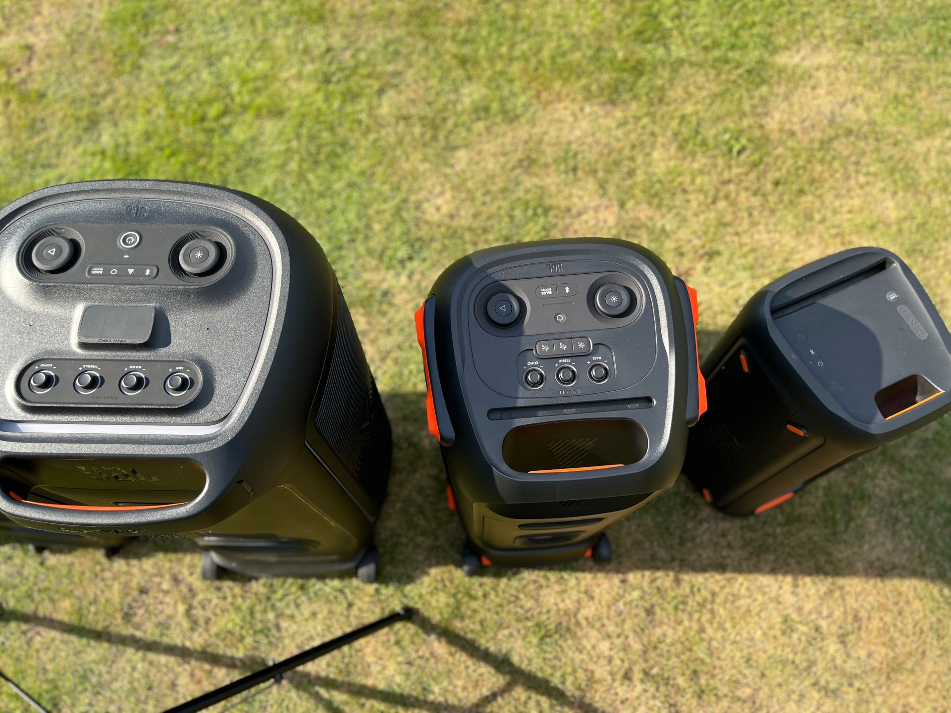 Drei schwarze, tragbare Party-Lautsprecher unterschiedlicher Größe stehen in einer Reihe auf einem Rasen.