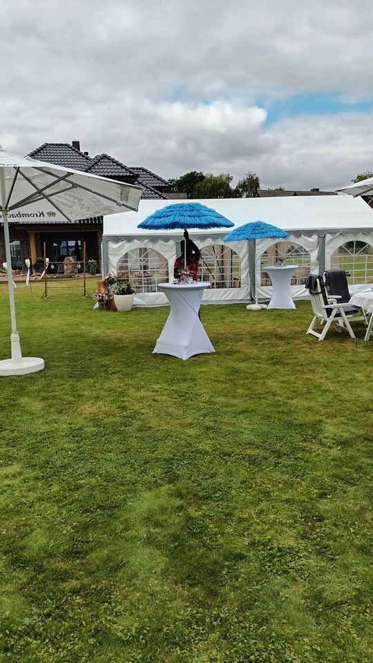 Eine Rasenfläche mit weißen Partyzelten, Stehtischen mit blauen Sonnenschirmen und weißen Stühlen für eine Veranstaltung im Freien.