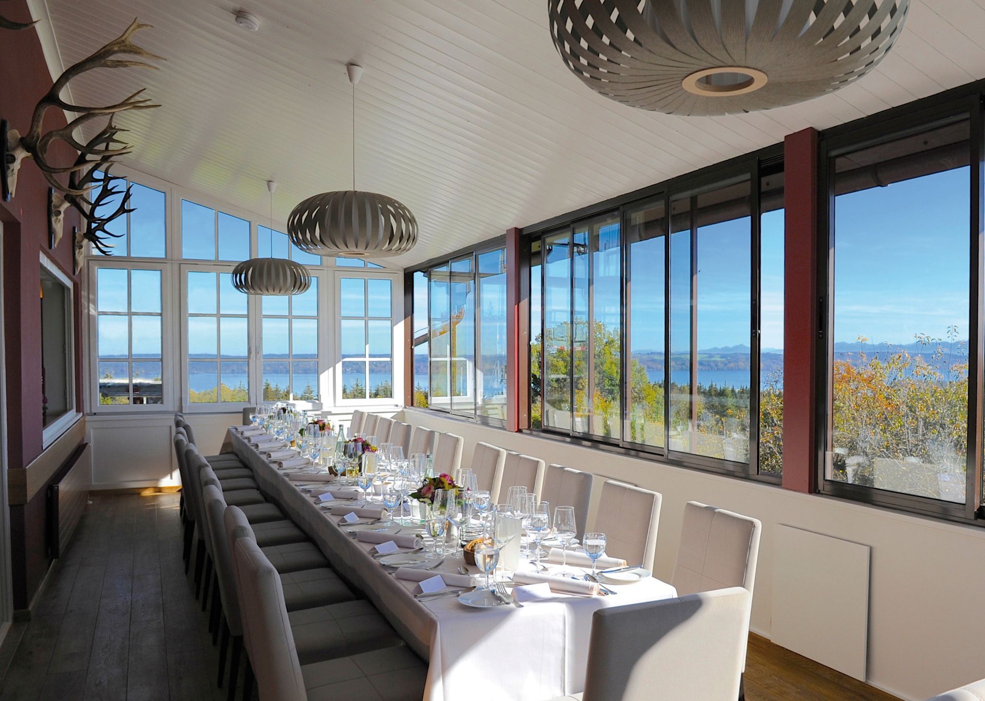 Elegantes Esszimmer mit einem langen Esstisch, modernen Stühlen und großen Fenstern mit Blick auf das helle Wasser