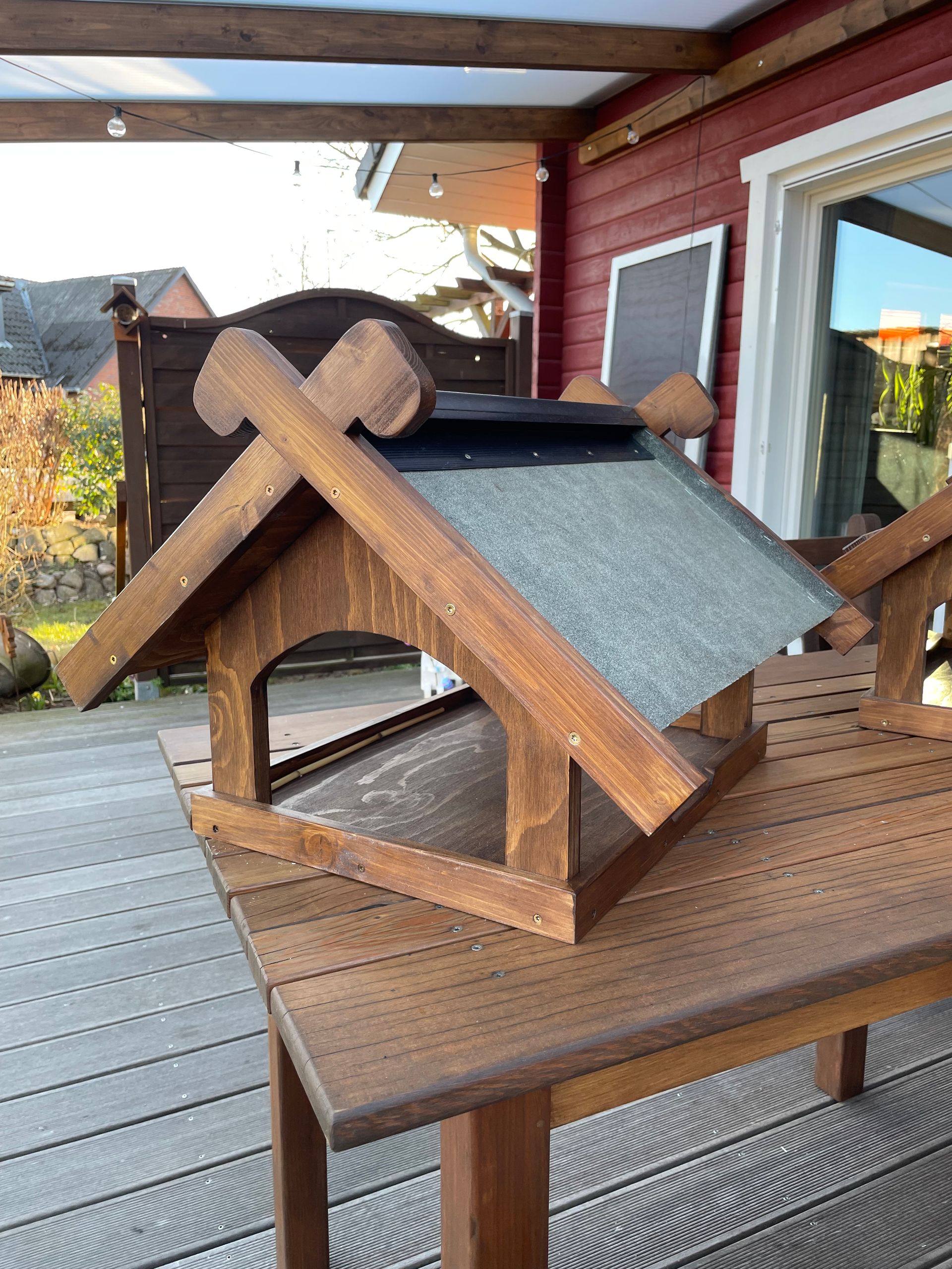Futterhaus „Niedersachsen“ aus Holz mit Dach, belegt mit Dachpappe inklusive stilisierter Pferdeköpfe am Giebel.