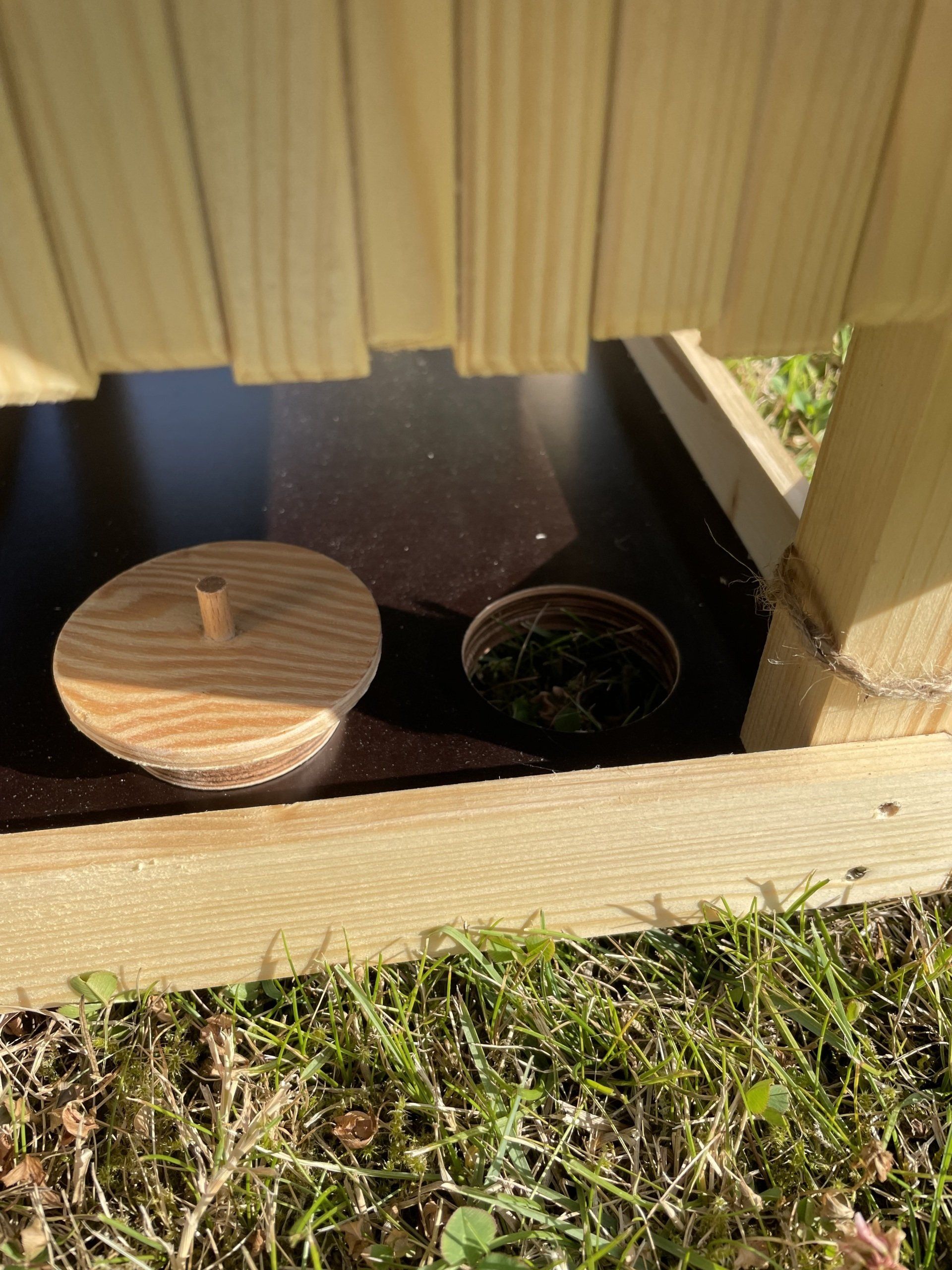 Futterhaus aus Fichtenholz mit Dach und Boden aus einer Siebdruckplatte. Fokus auf Loch und Deckel zum Säubern