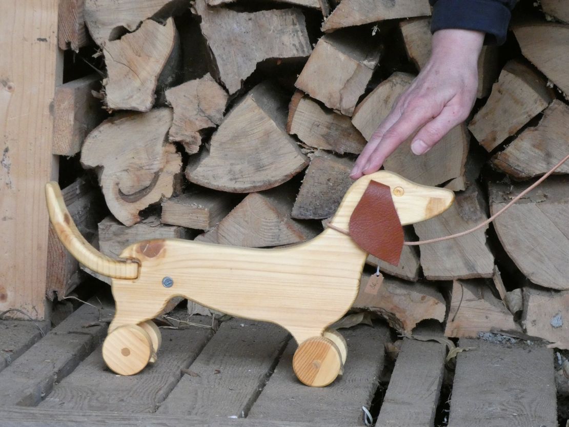 Handgefertigter Dackel auch Holz mit hängenden Ohren aus Leder. Eine Hand streichelt über den Dackelkopf.
