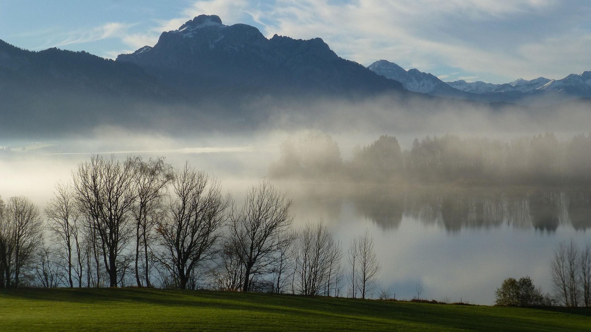 Nebliger See mit Spiegelungen. Segelboote liegen vor Anker. Neblig, blau und friedlich.