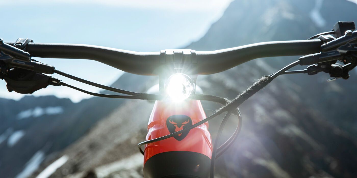 Nahaufnahme eines Rotwild Leihmountainbike-Lenkers, helles Licht, im Hintergrund Berge.