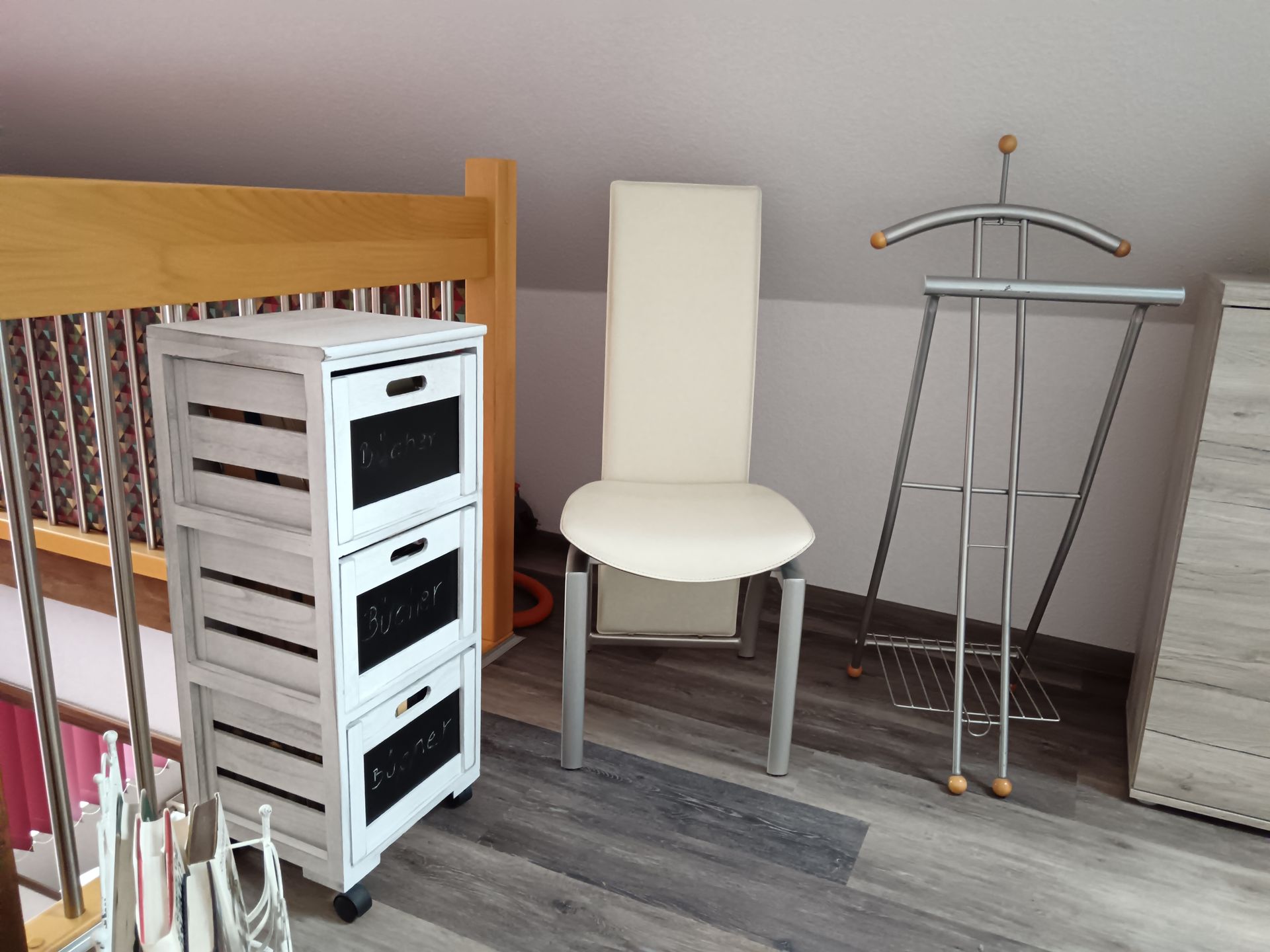 Weißer Schrank mit Schubladen, Stuhl und Kleiderständer in einem Zimmer mit Dachschräge.