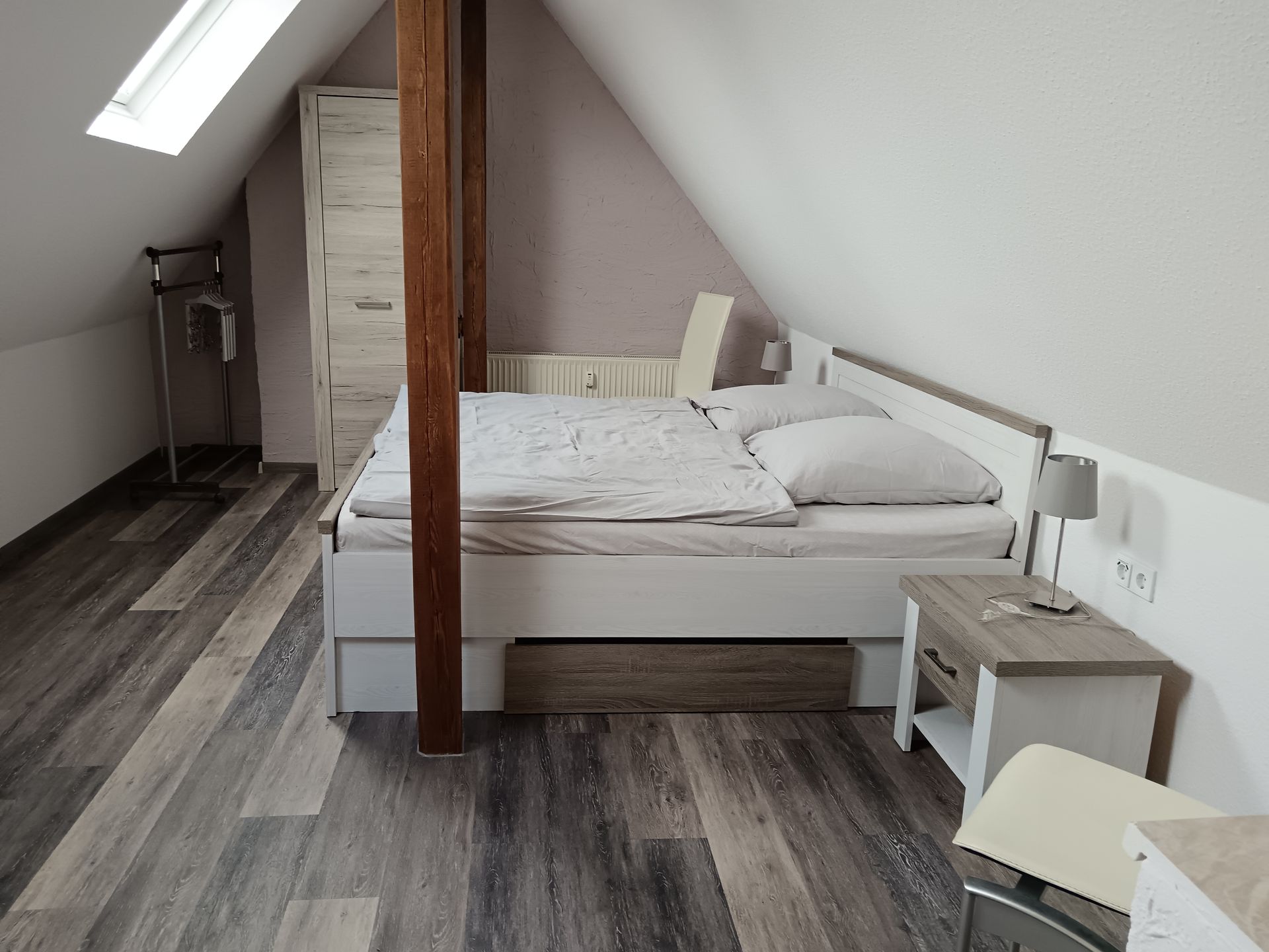 Schlafzimmer mit Bett, Nachttisch, hölzernem Stützbalken und Dachschräge.