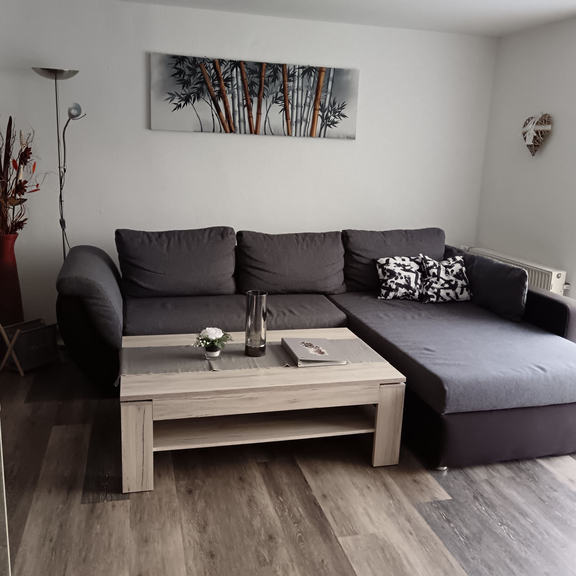 Wohnzimmer mit grauem Ecksofa, hellem Holz-Couchtisch und Bambuskunstwerk.