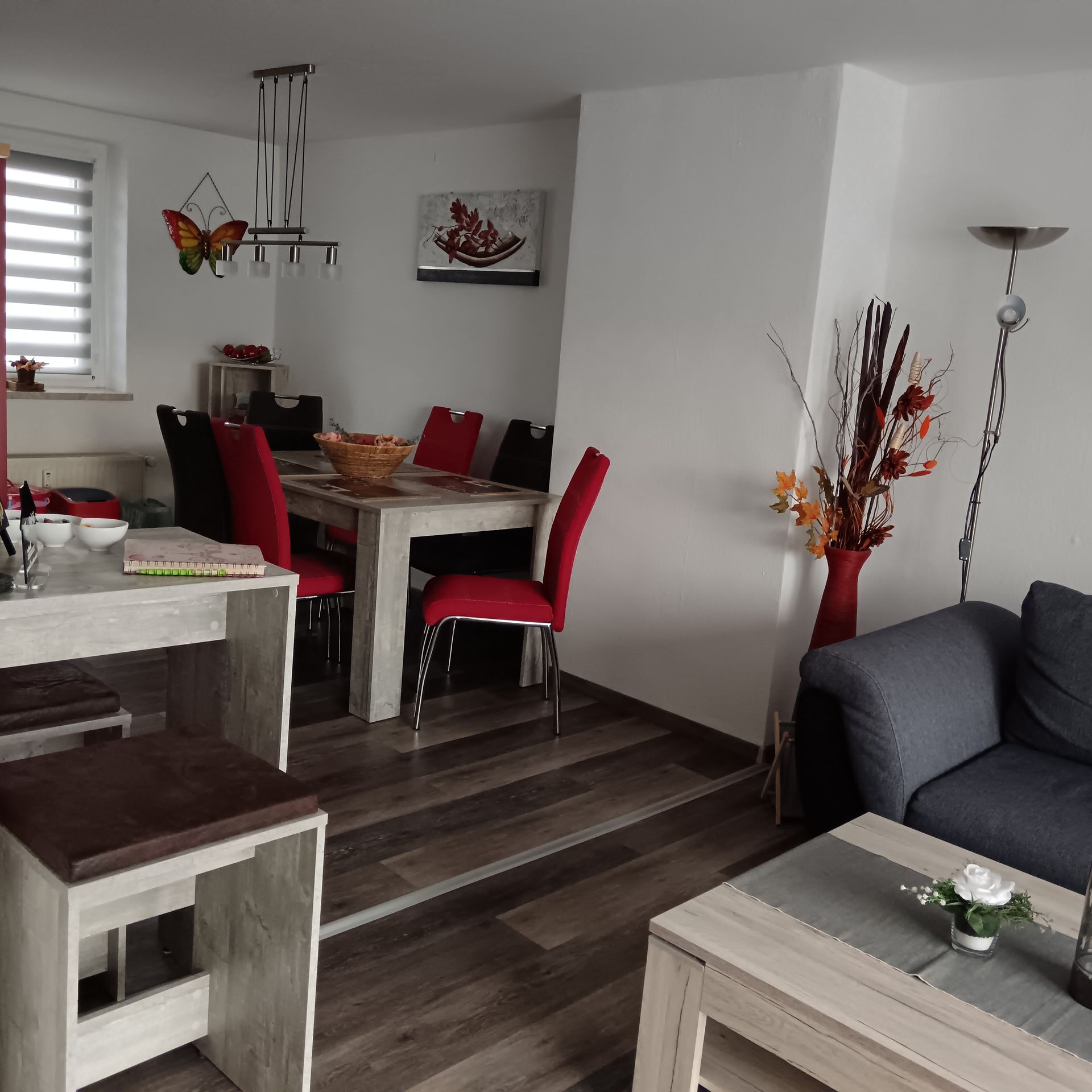 Wohn-/Esszimmer mit Tisch, Stühlen, Sofa und Holzboden. Rote und schwarze Akzente.